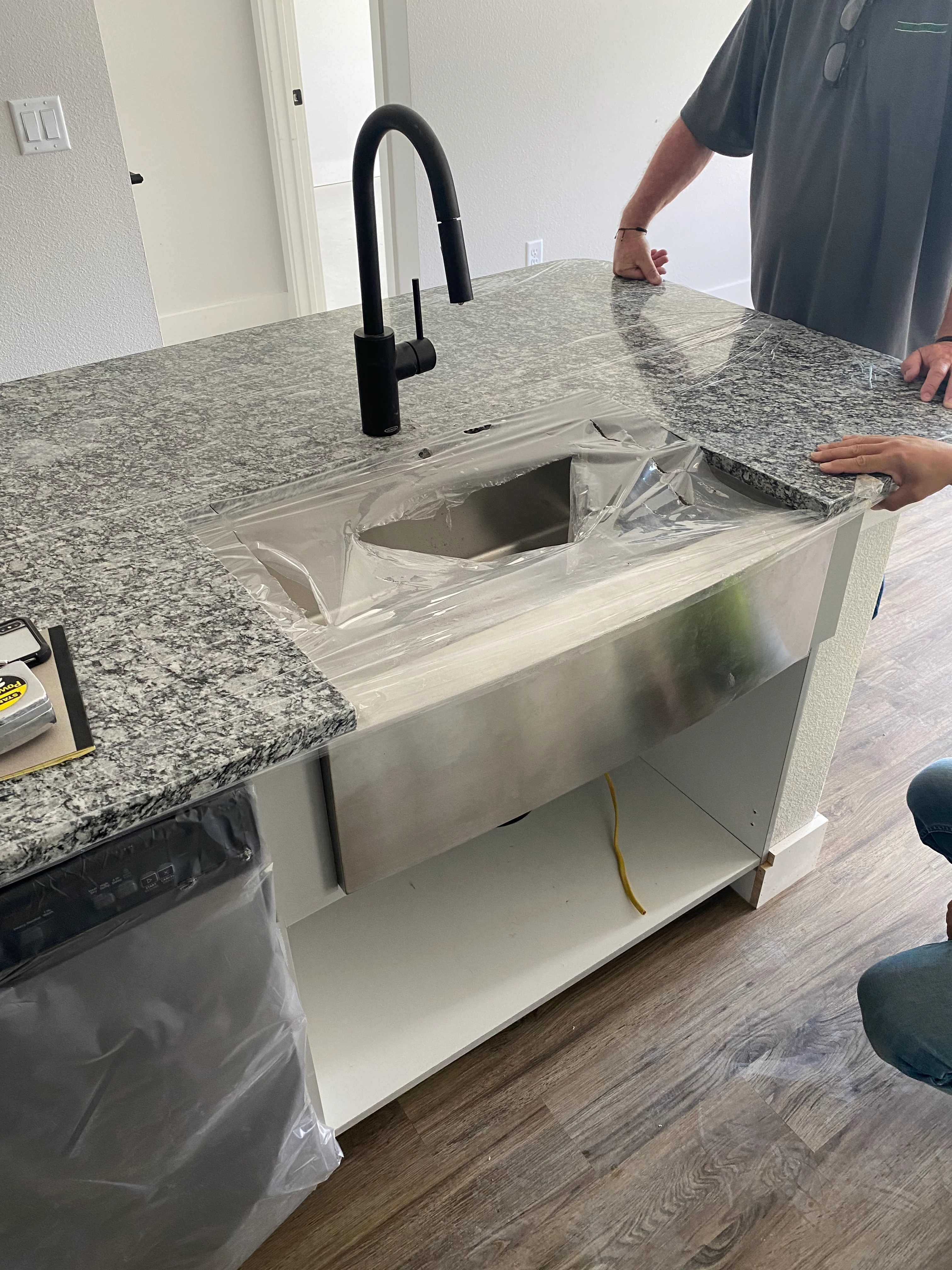 Stainless steel farmhouse sink with black faucet installed in granite countertop