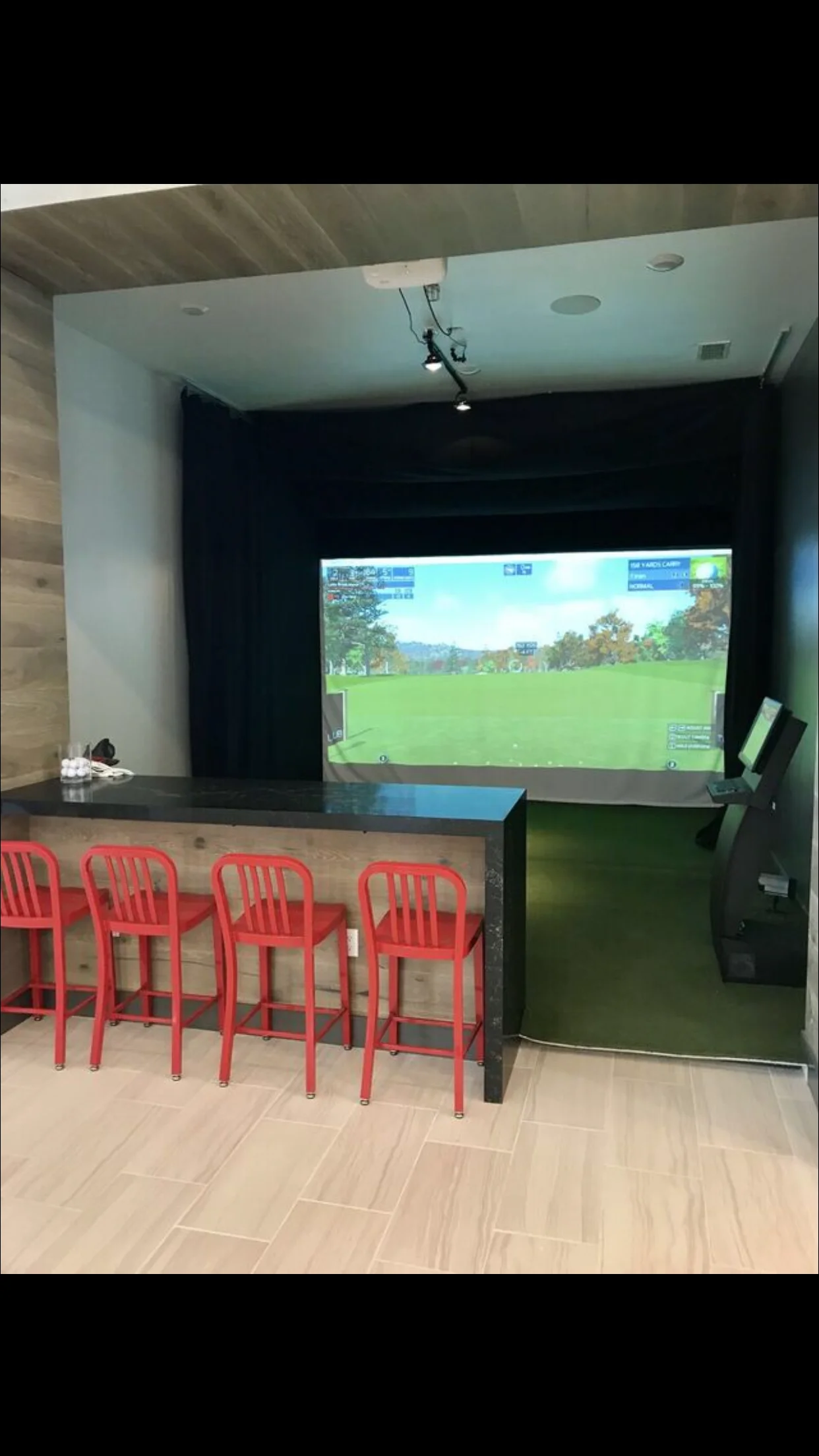 Golf simulator room with projection screen, red bar stools, and concrete counter
