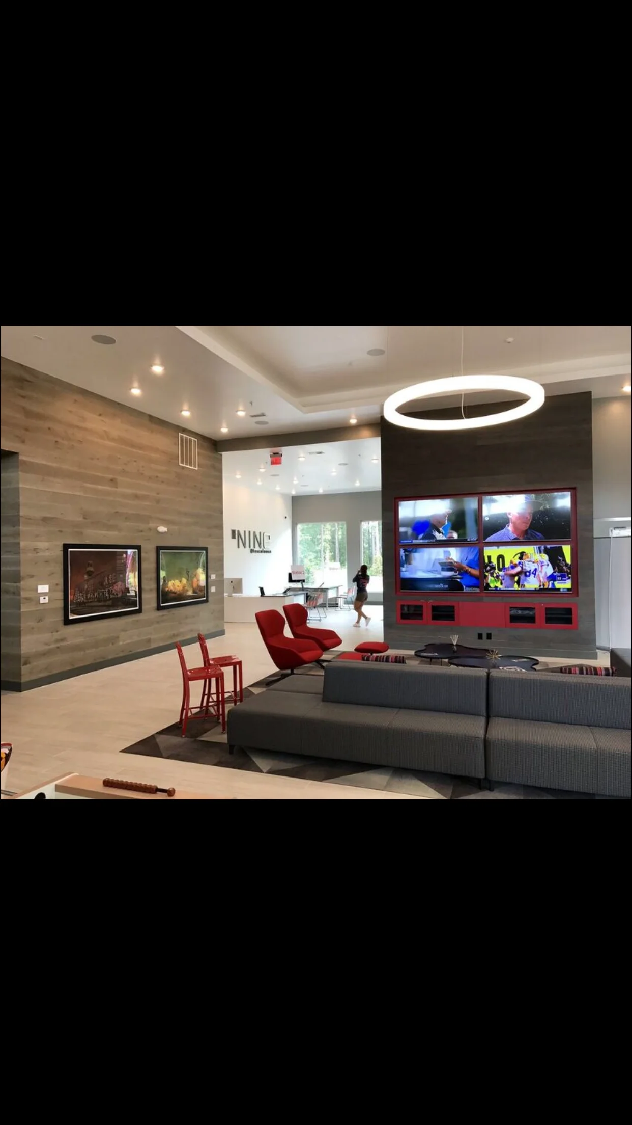 Modern media room with wood accent wall, gray sectional sofa, red chairs, and multi-screen TV display
