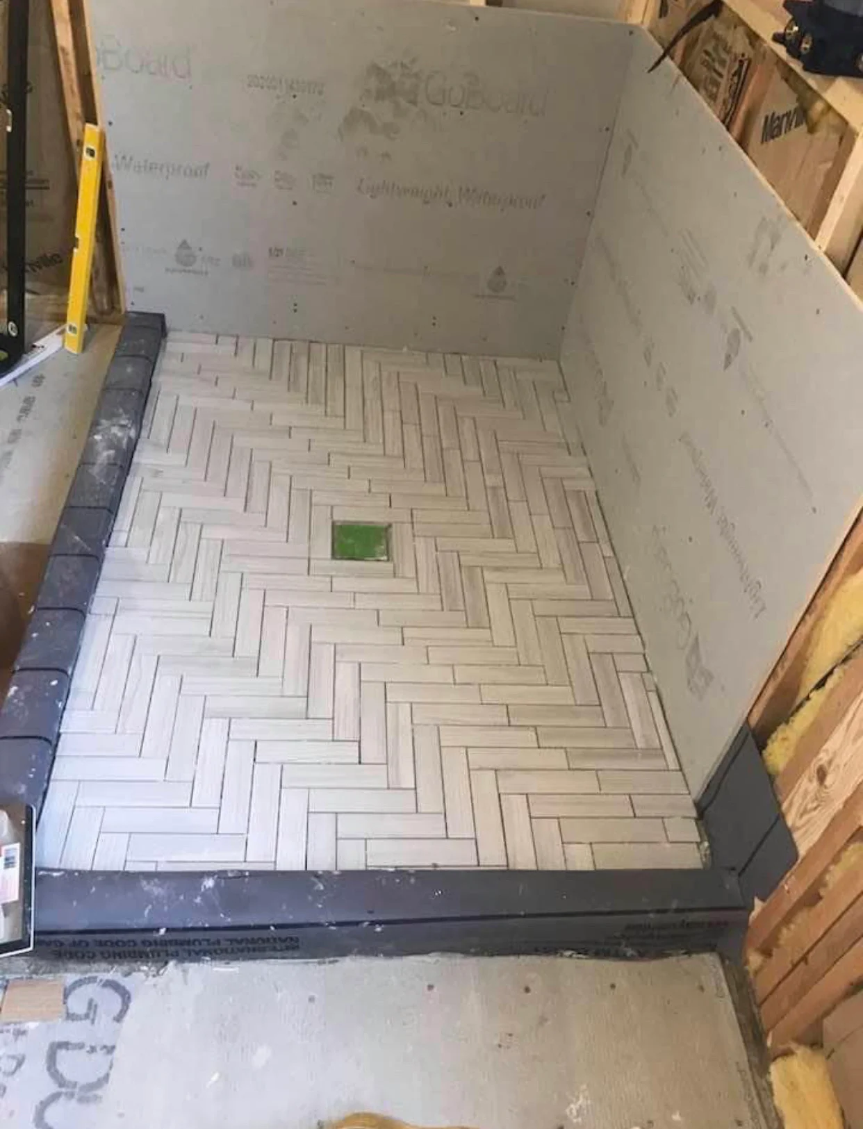 Herringbone pattern tile installation in progress with light tiles and waterproof backing