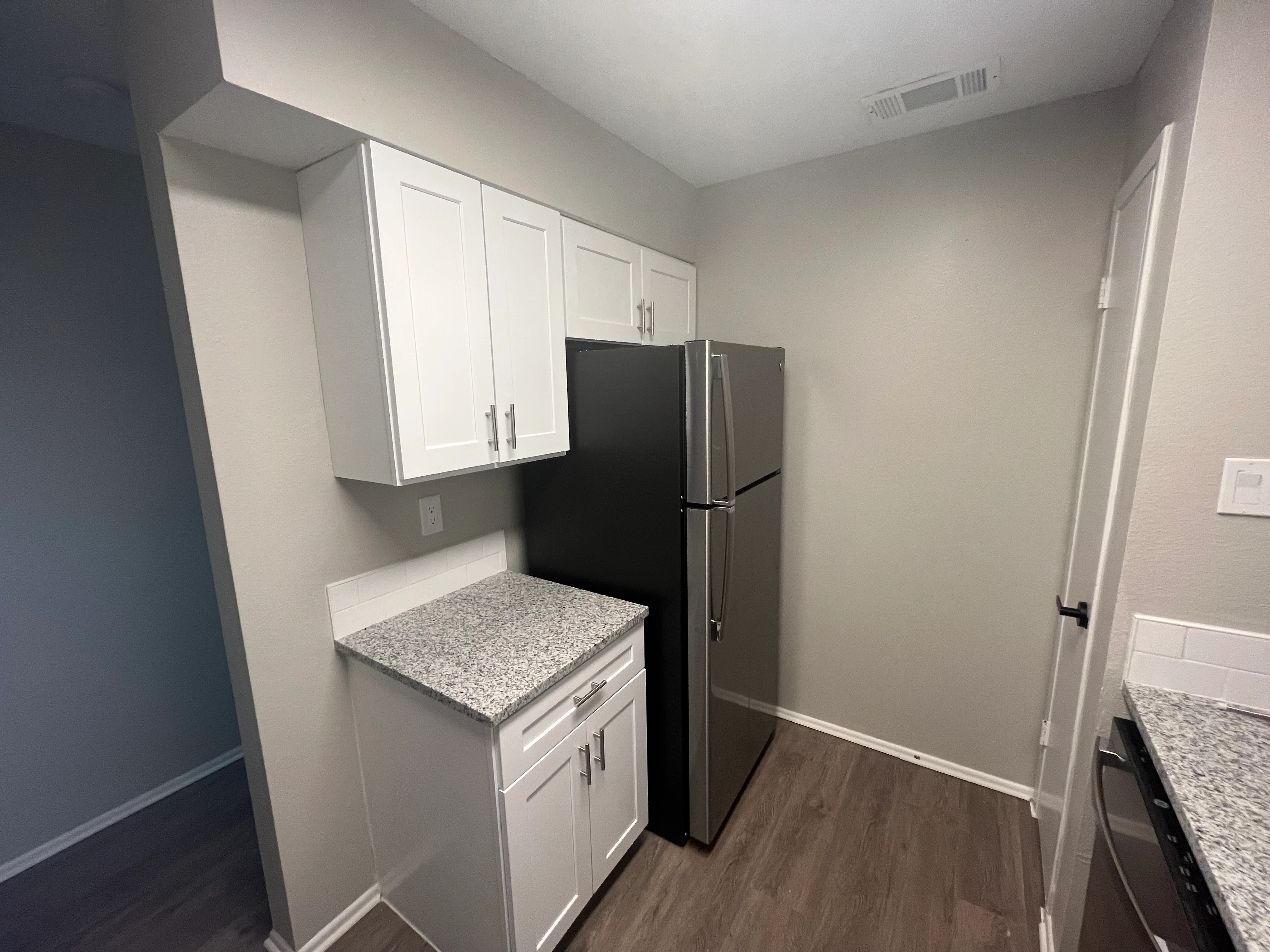 Modern kitchen with white cabinets, granite counters, and black stainless steel refrigerator