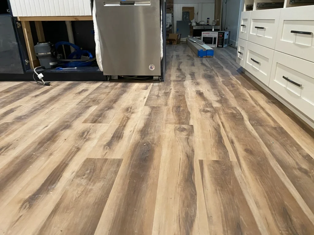 Newly installed luxury vinyl plank flooring in kitchen with wood-look finish and white cabinetry