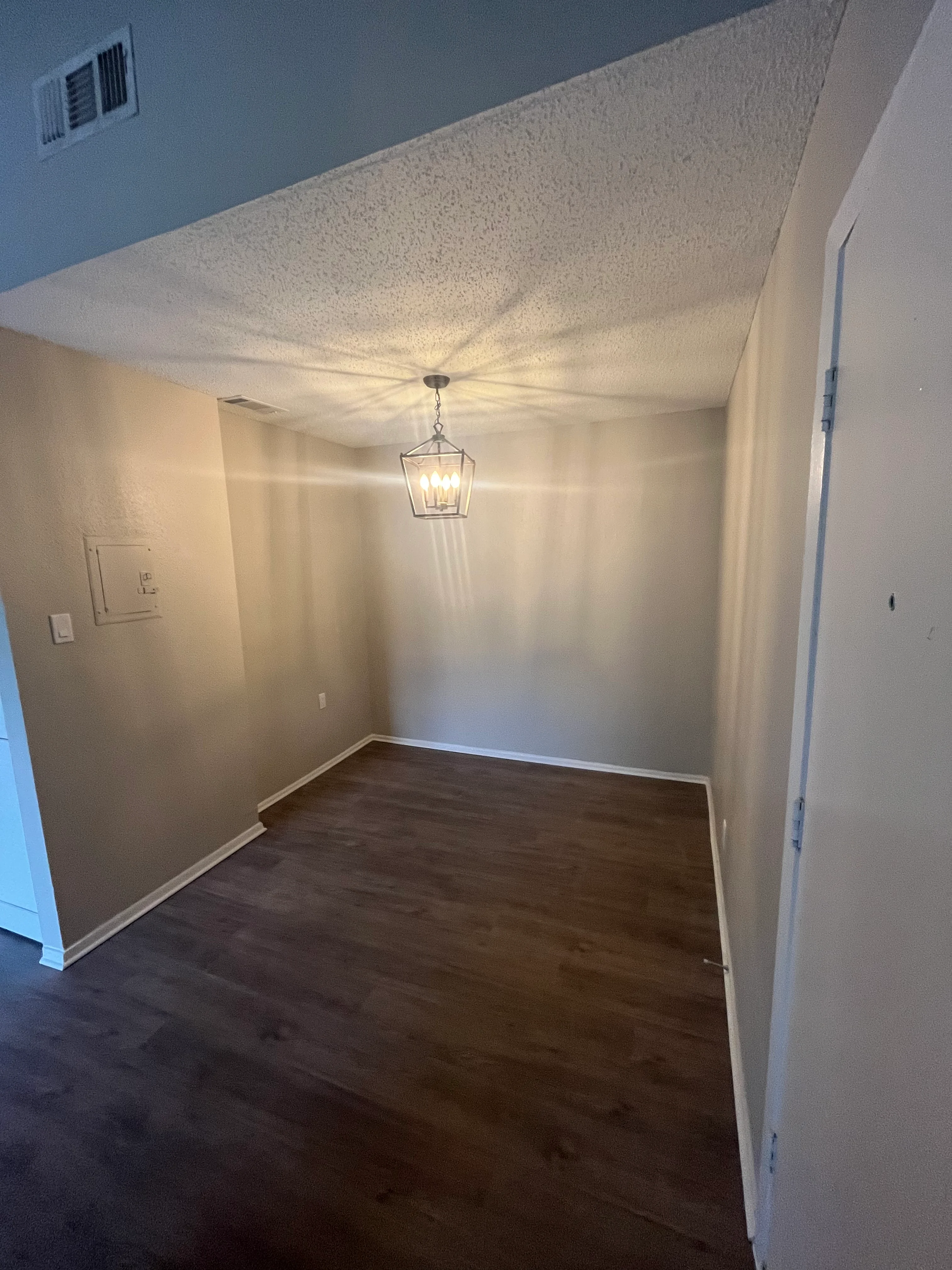 Newly renovated interior room with textured ceiling, painted walls, hardwood flooring, and pendant light