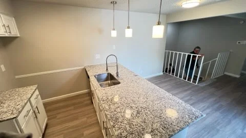 Modern kitchen with granite counters, pendant lights, and hardwood floors opening to living area