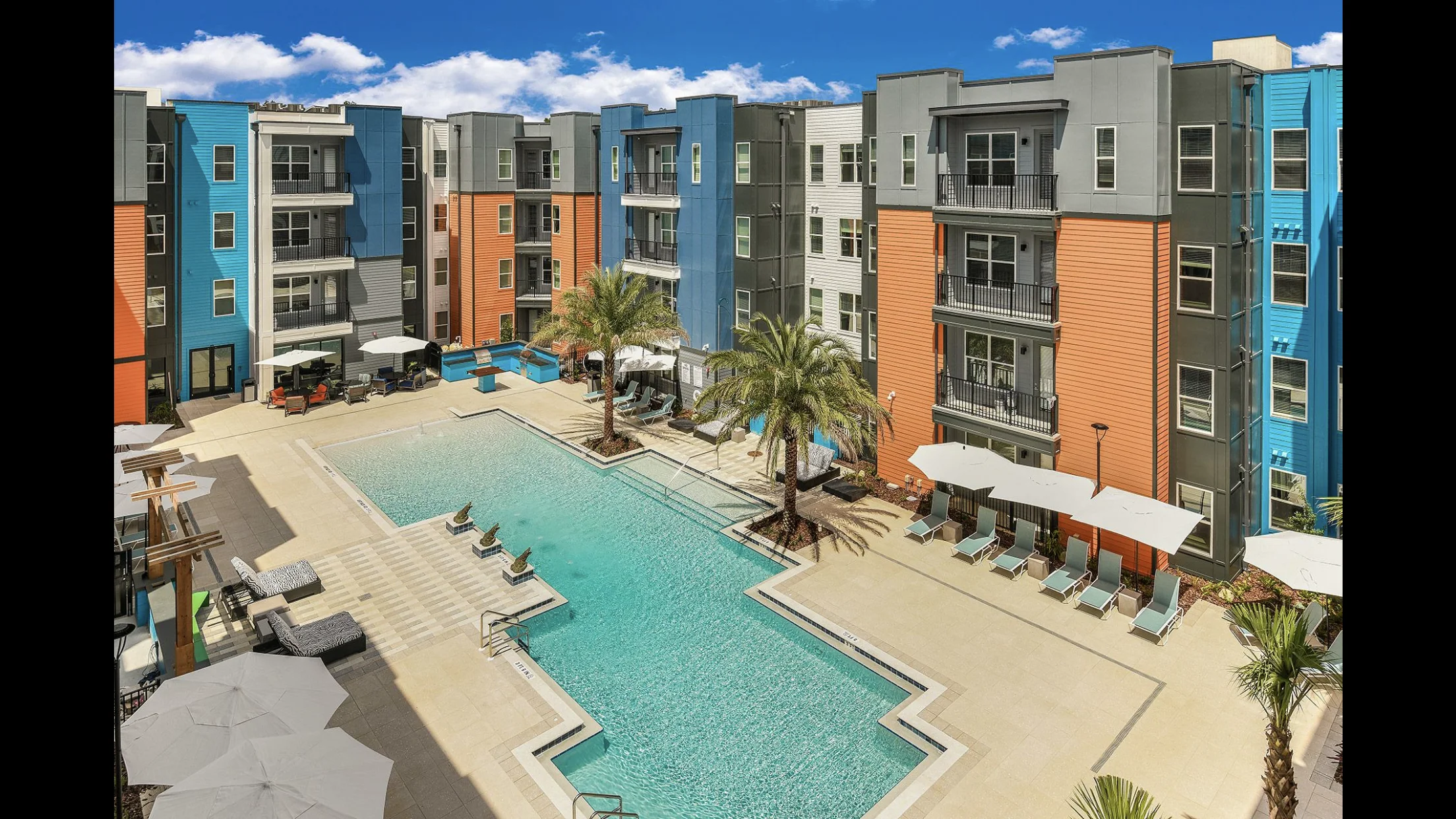 Aerial view of modern apartment complex with pools, palm trees, and colorful building facades