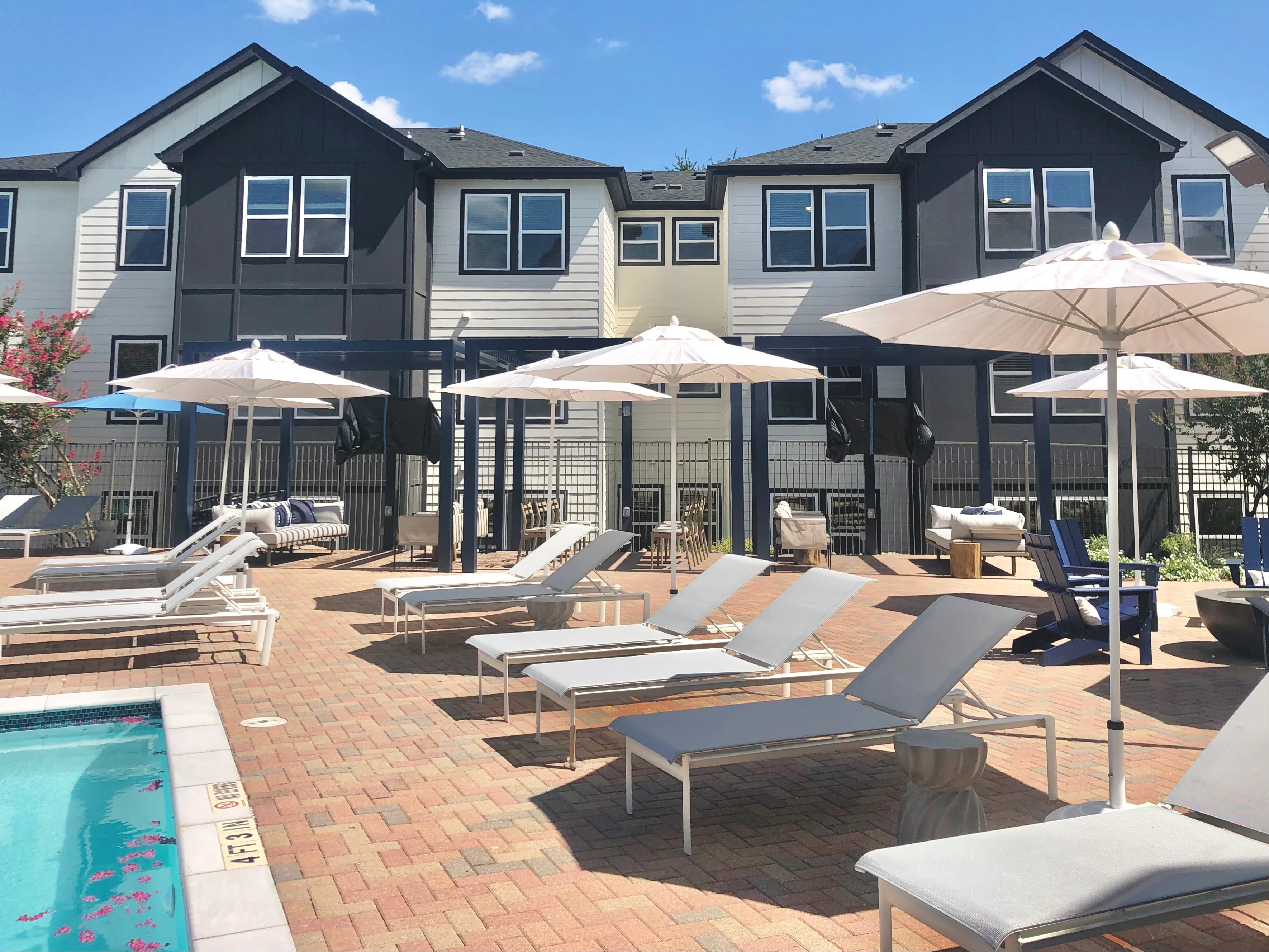 Multi-unit townhomes with pool, lounge chairs, and umbrellas in sunny courtyard
