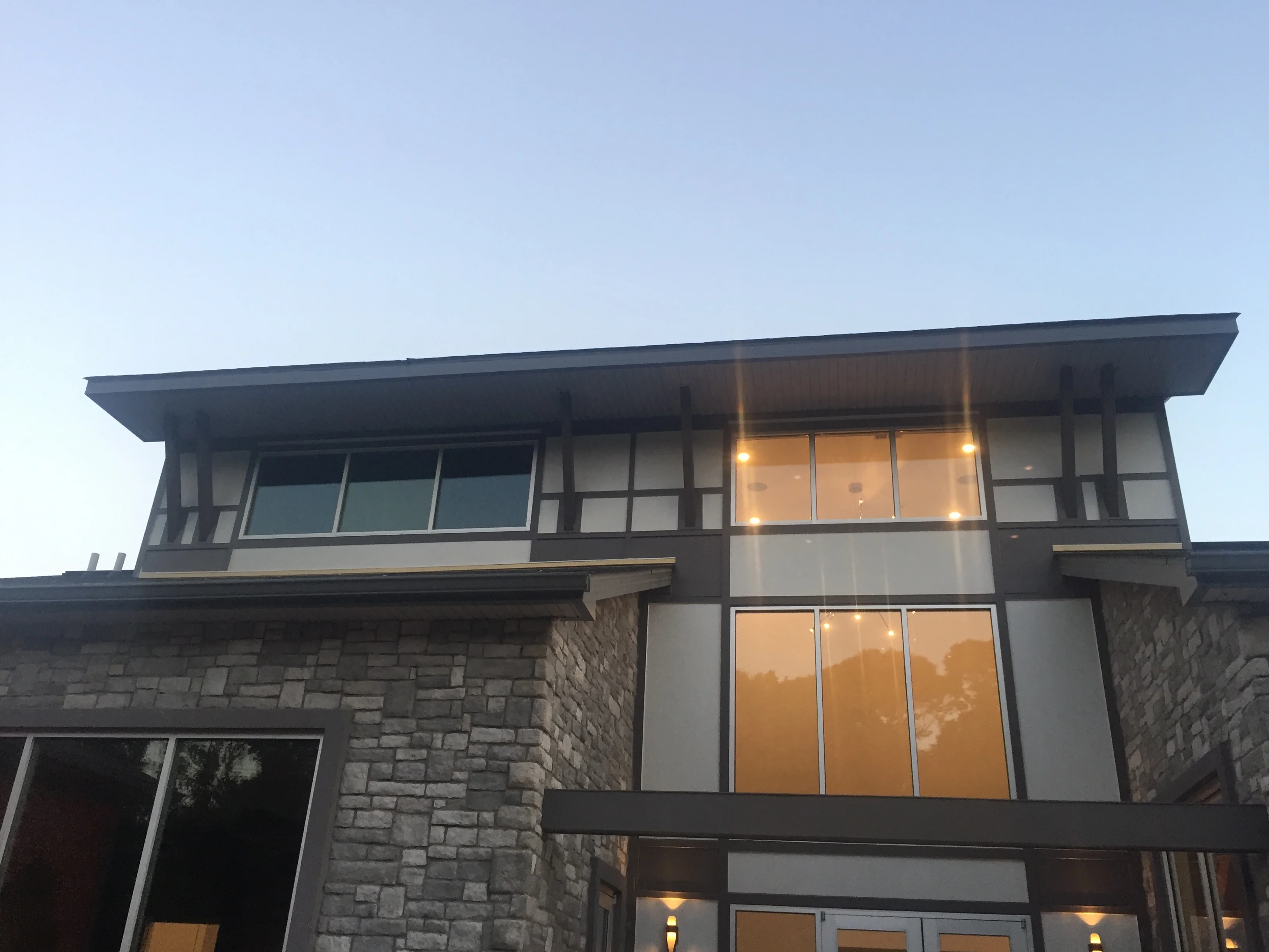 Modern two-story home addition with stone base, dark metal framing, and large windows at dusk