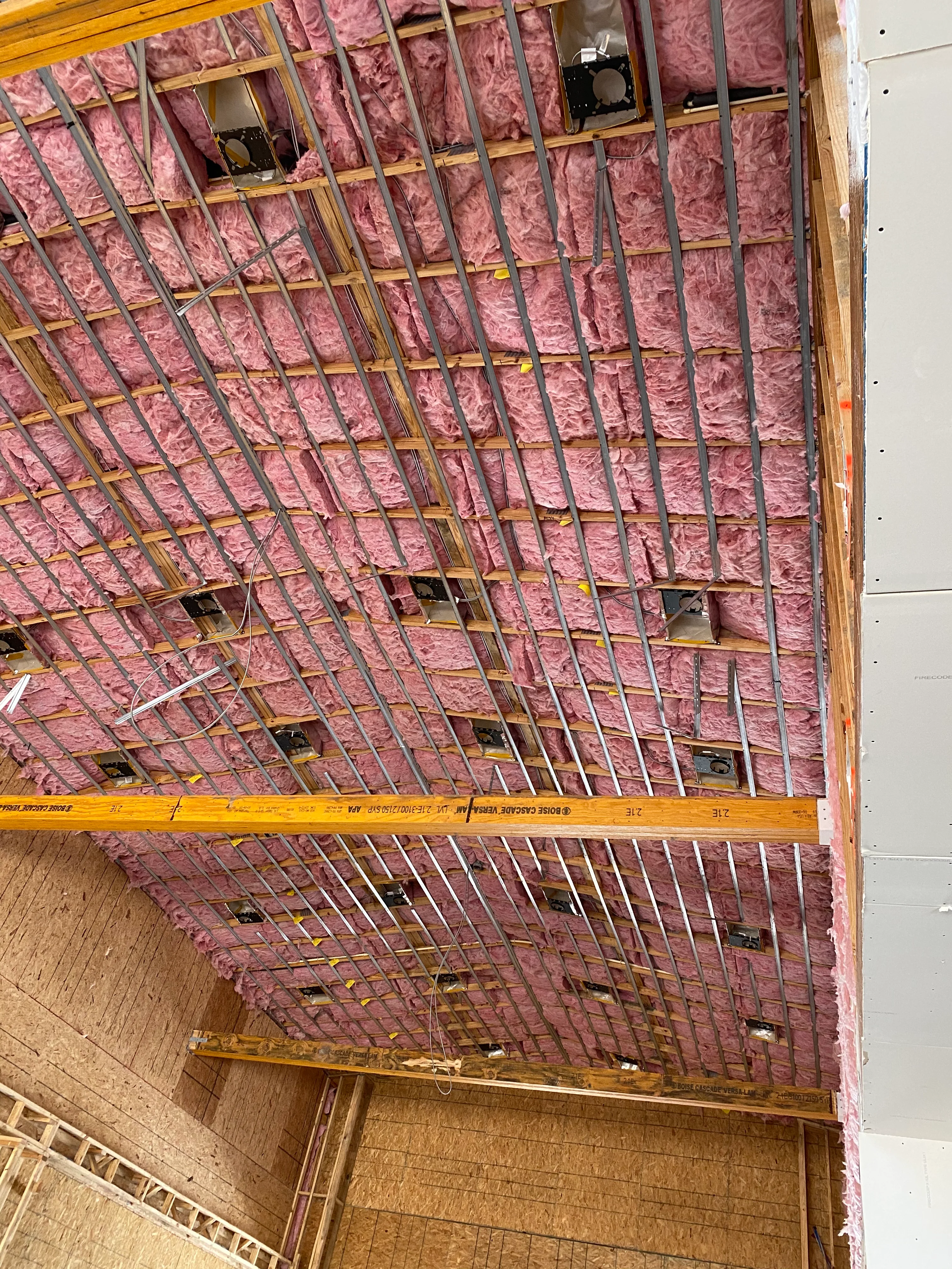 Pink fiberglass insulation installed between wooden ceiling joists with metal bracing