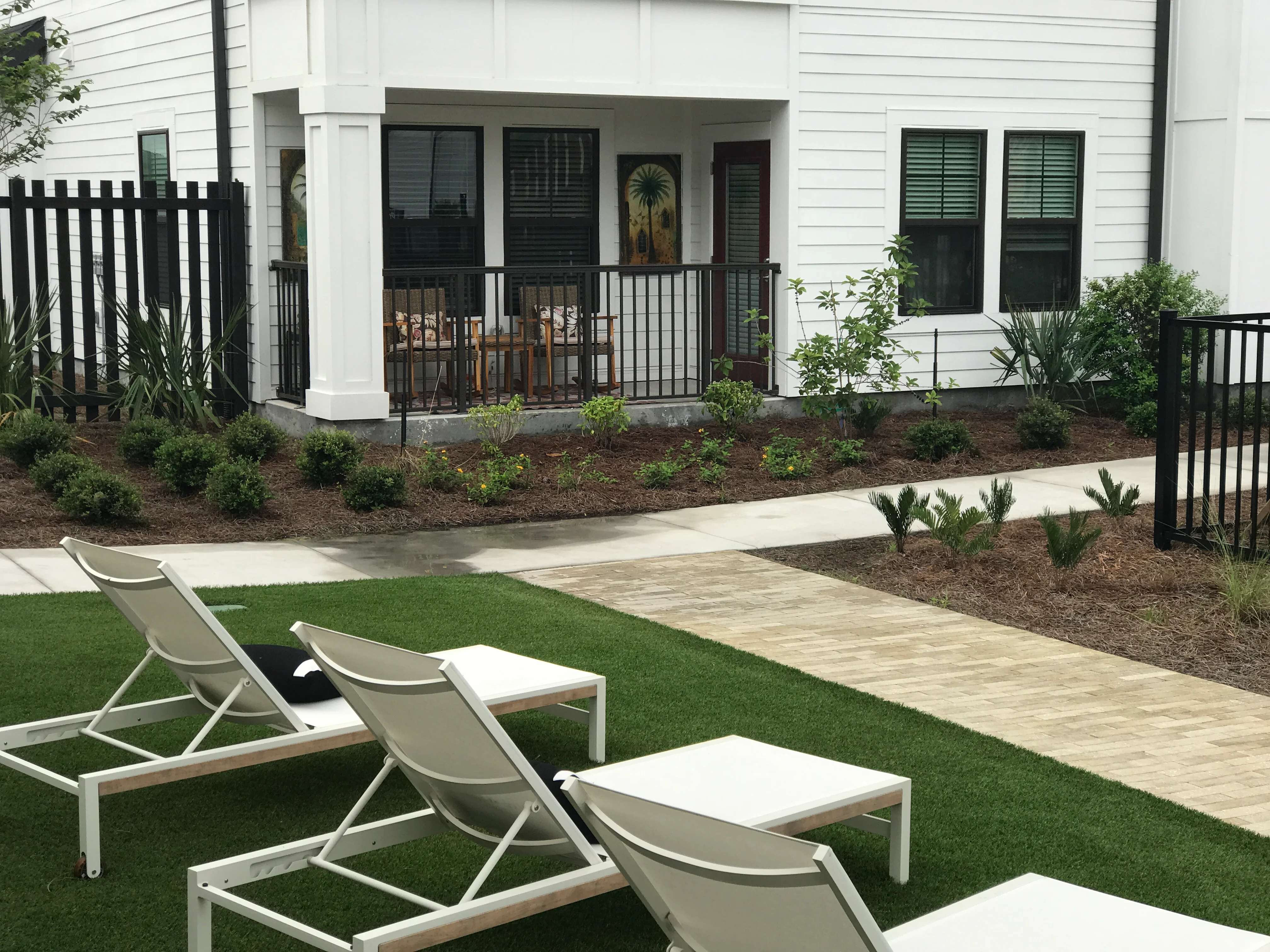 Modern backyard with synthetic turf, paver walkway, black metal railings, and landscape plantings