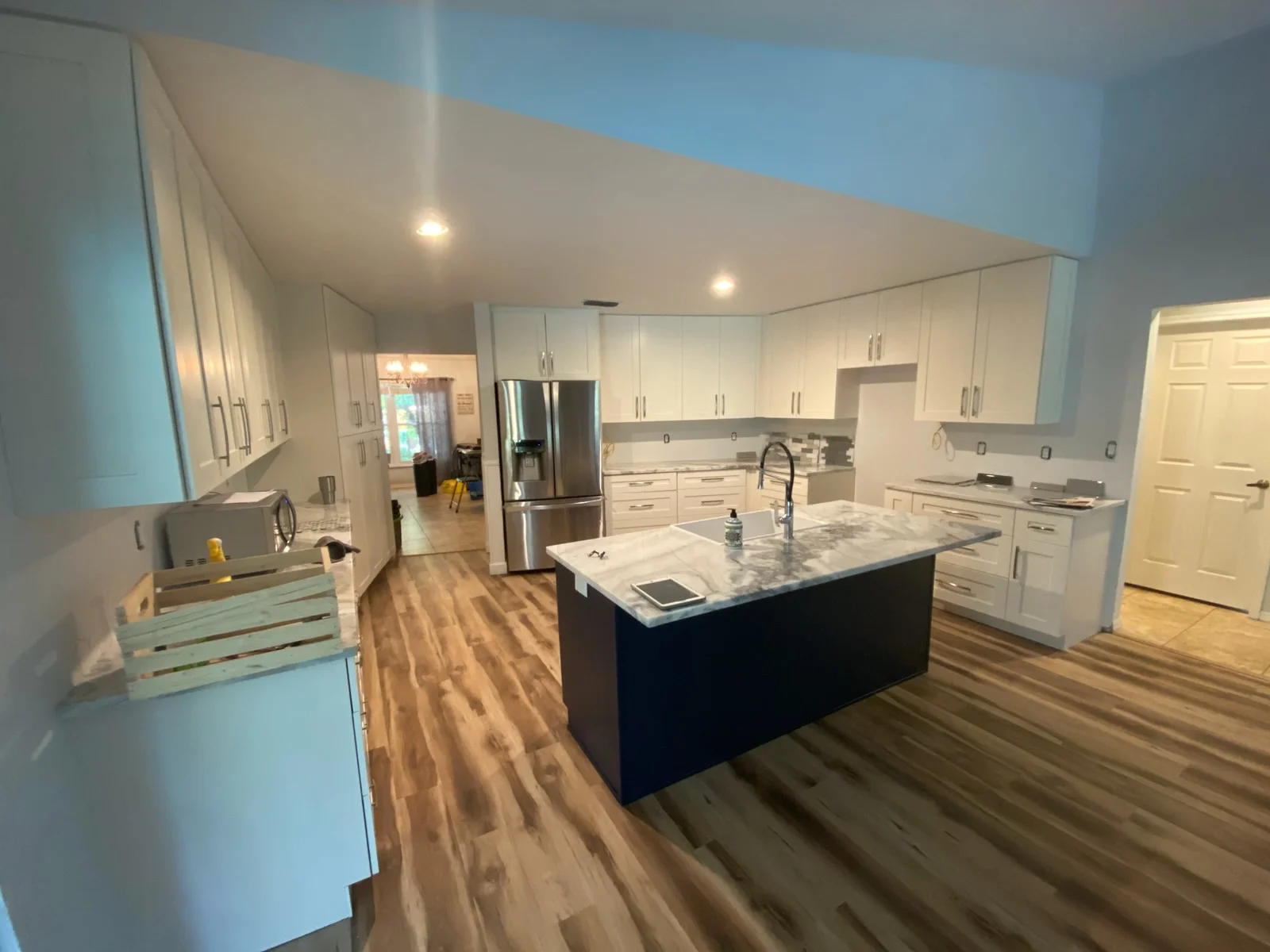 Modern kitchen with white cabinets, dark island, marble counters, and stainless steel appliances