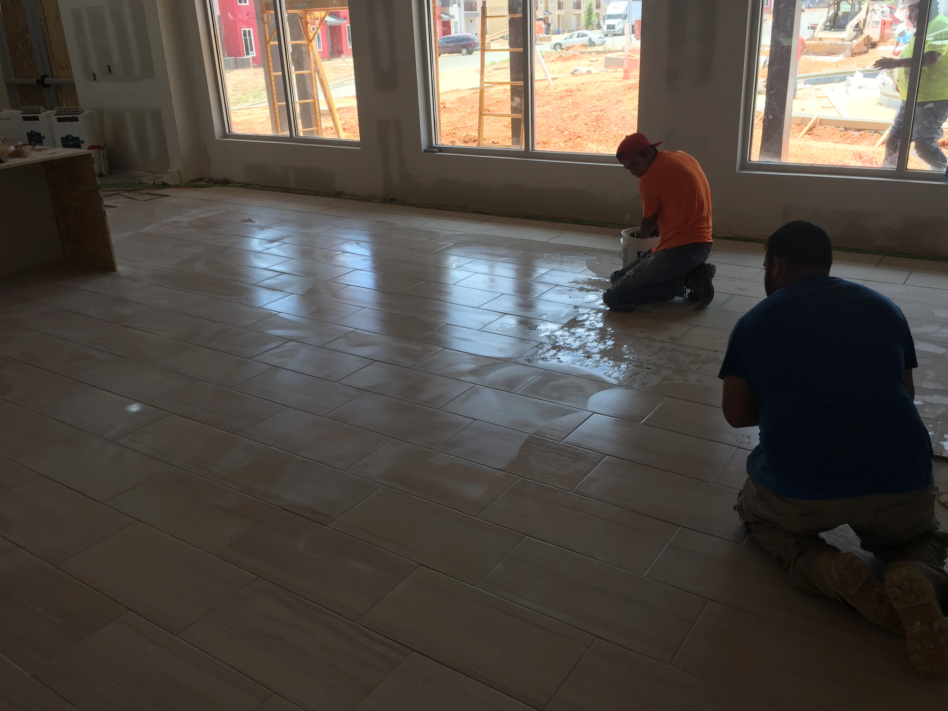 Workers installing ceramic tile flooring in commercial space with large windows