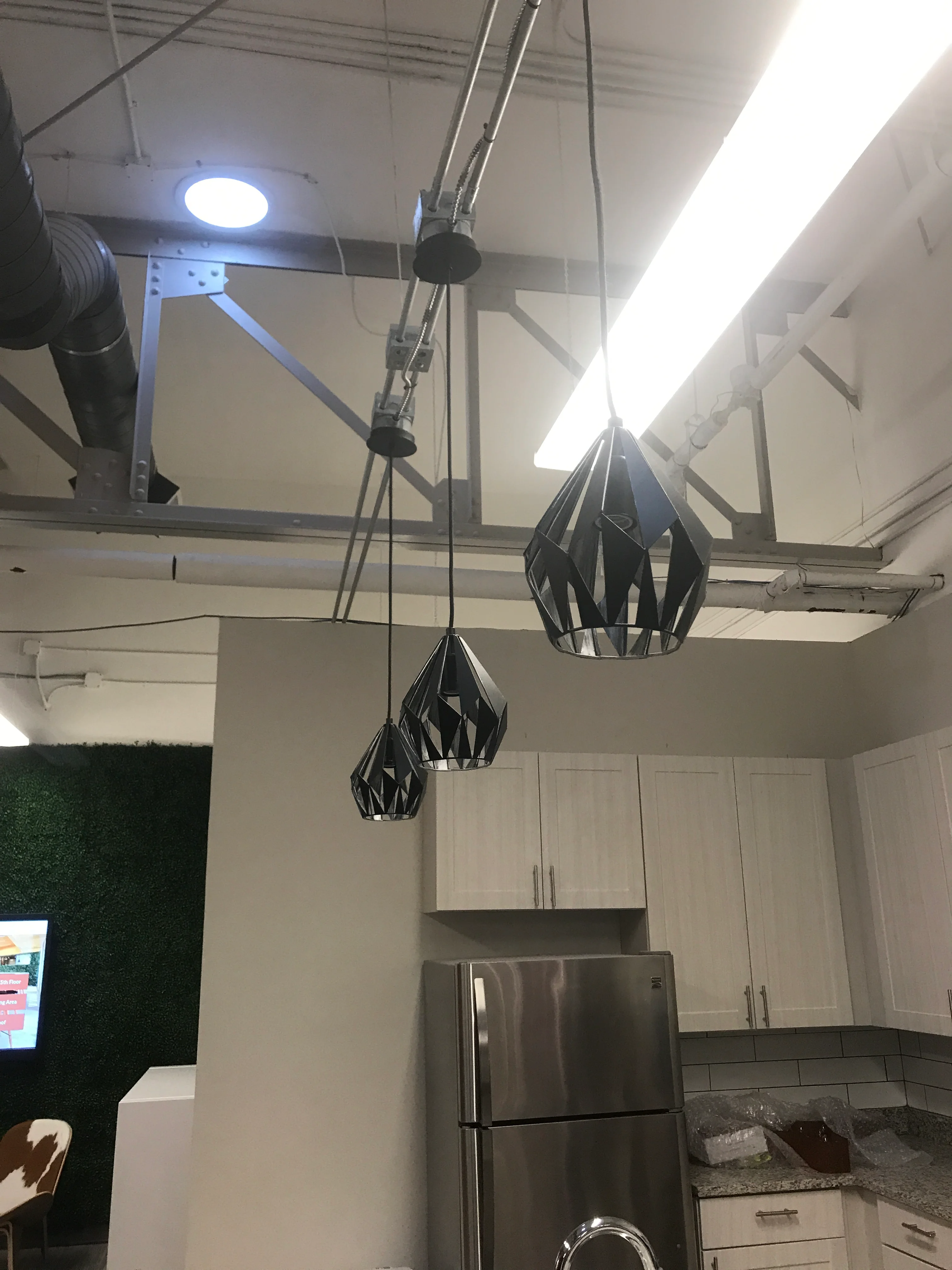 Modern kitchen with LED ceiling lights and black geometric pendant fixtures above stainless steel appliances