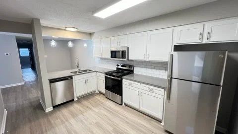 Modern kitchen with white cabinets, stainless steel appliances, and wood-look flooring