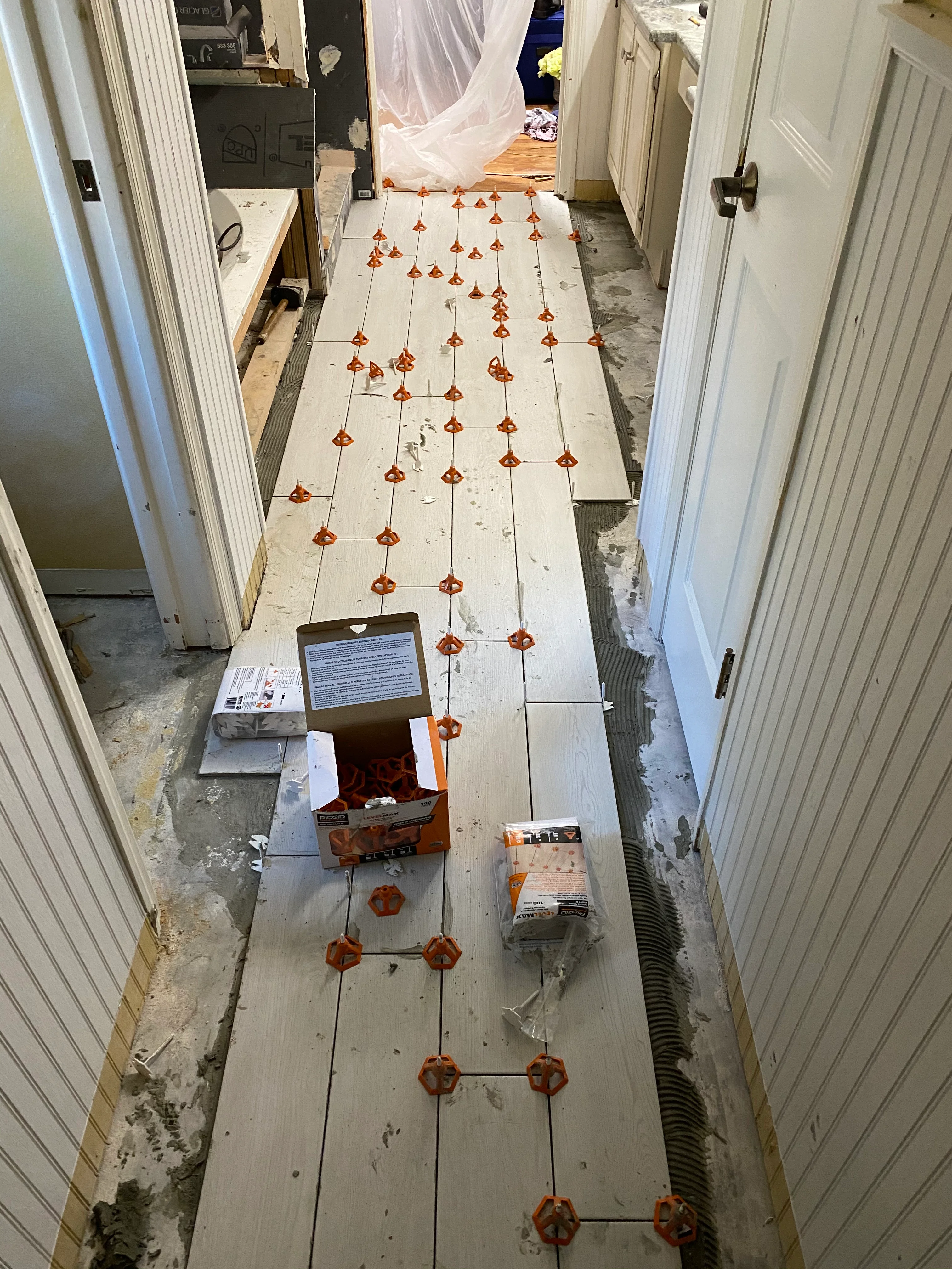 Bathroom tile layout with orange spacers marking grout lines on white subfloor