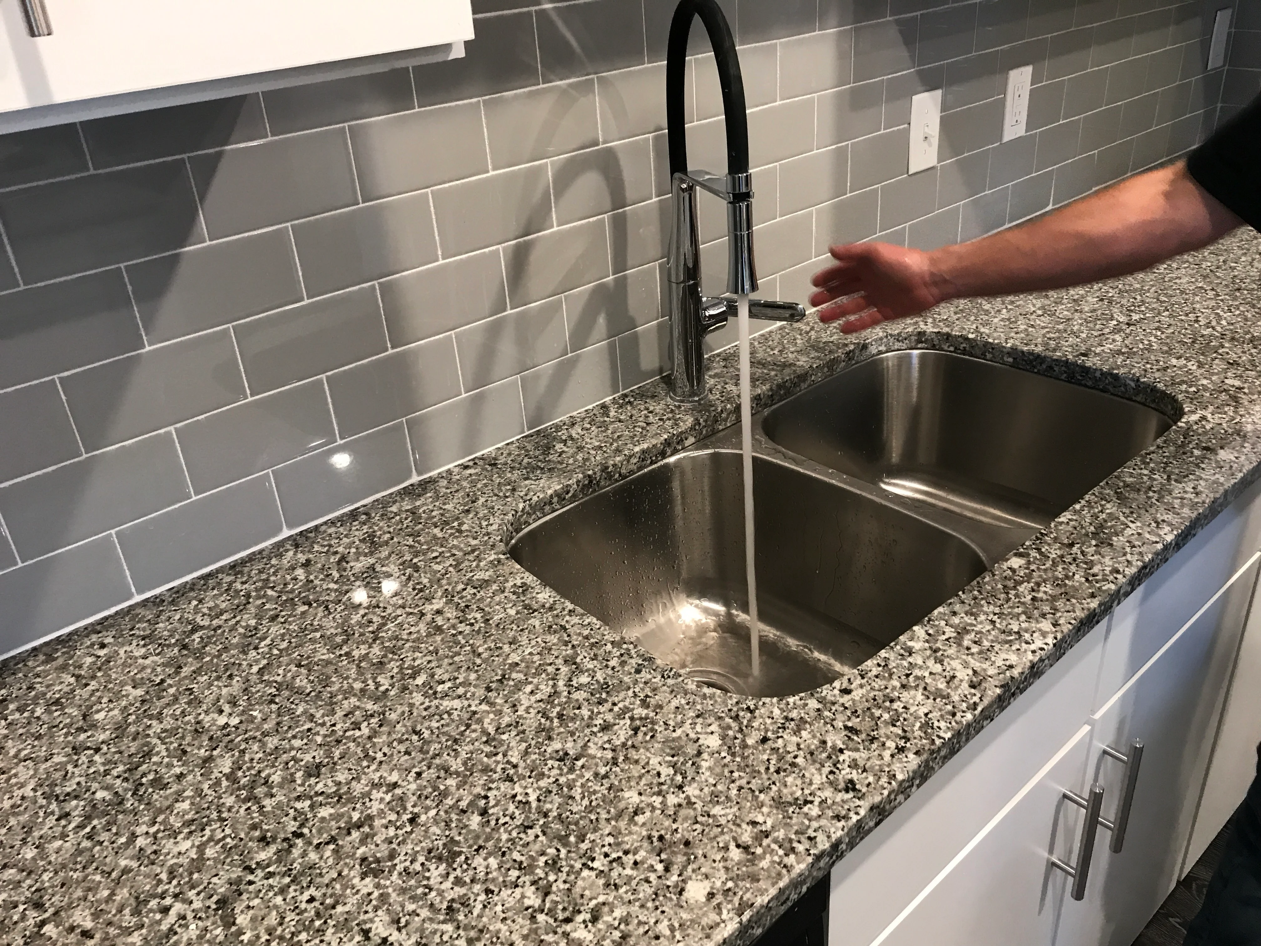 Modern kitchen sink with gray quartz countertop, stainless steel faucet, and gray subway tile backsplash