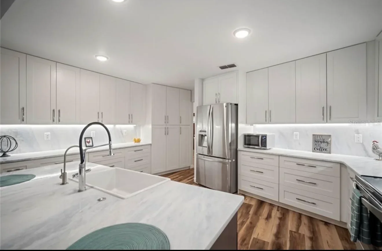 Modern kitchen with white cabinets, quartz counters, stainless steel appliances, and wood flooring
