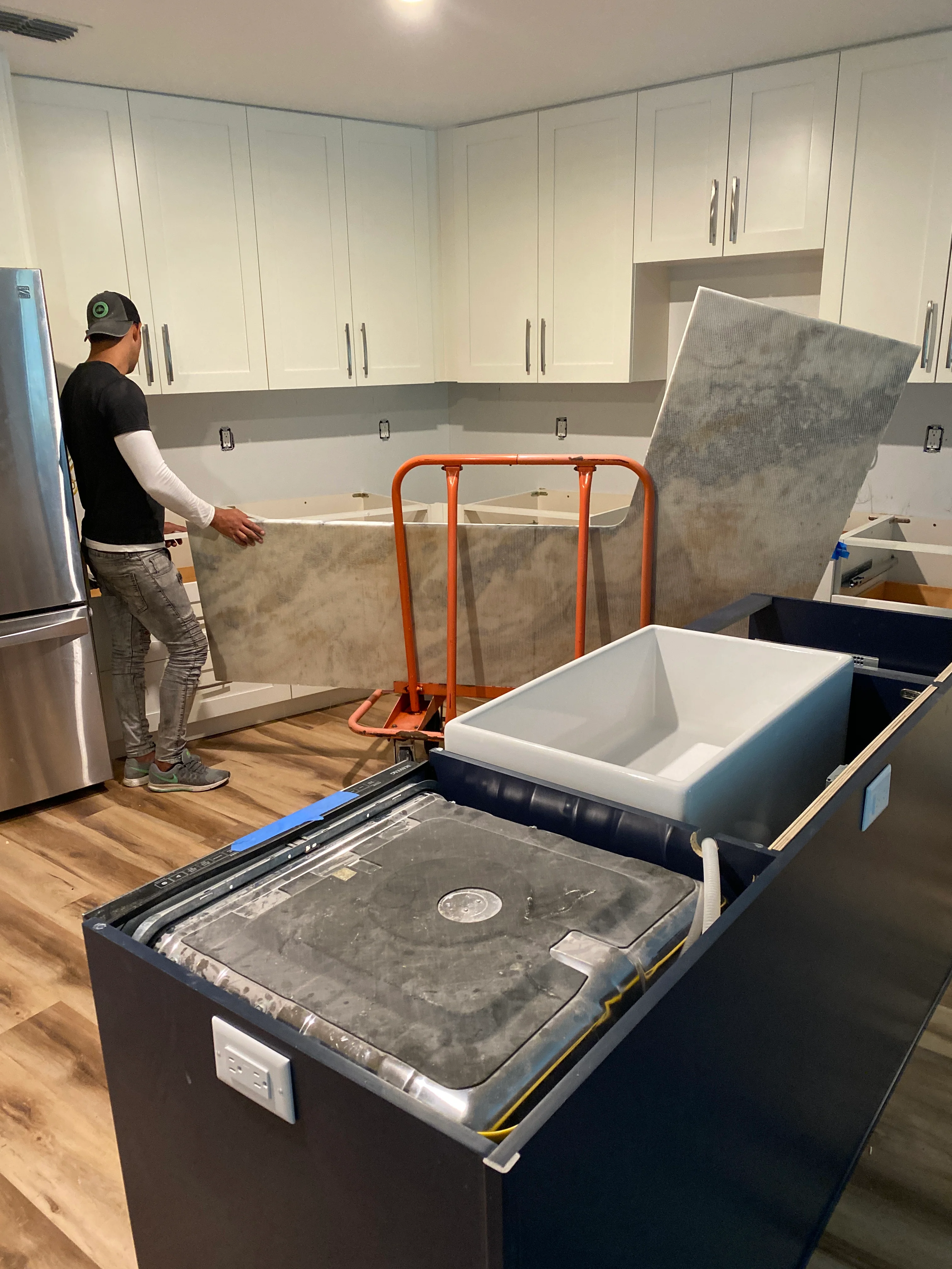 Kitchen remodeling in progress with white cabinets, gray countertops, and new sink installation