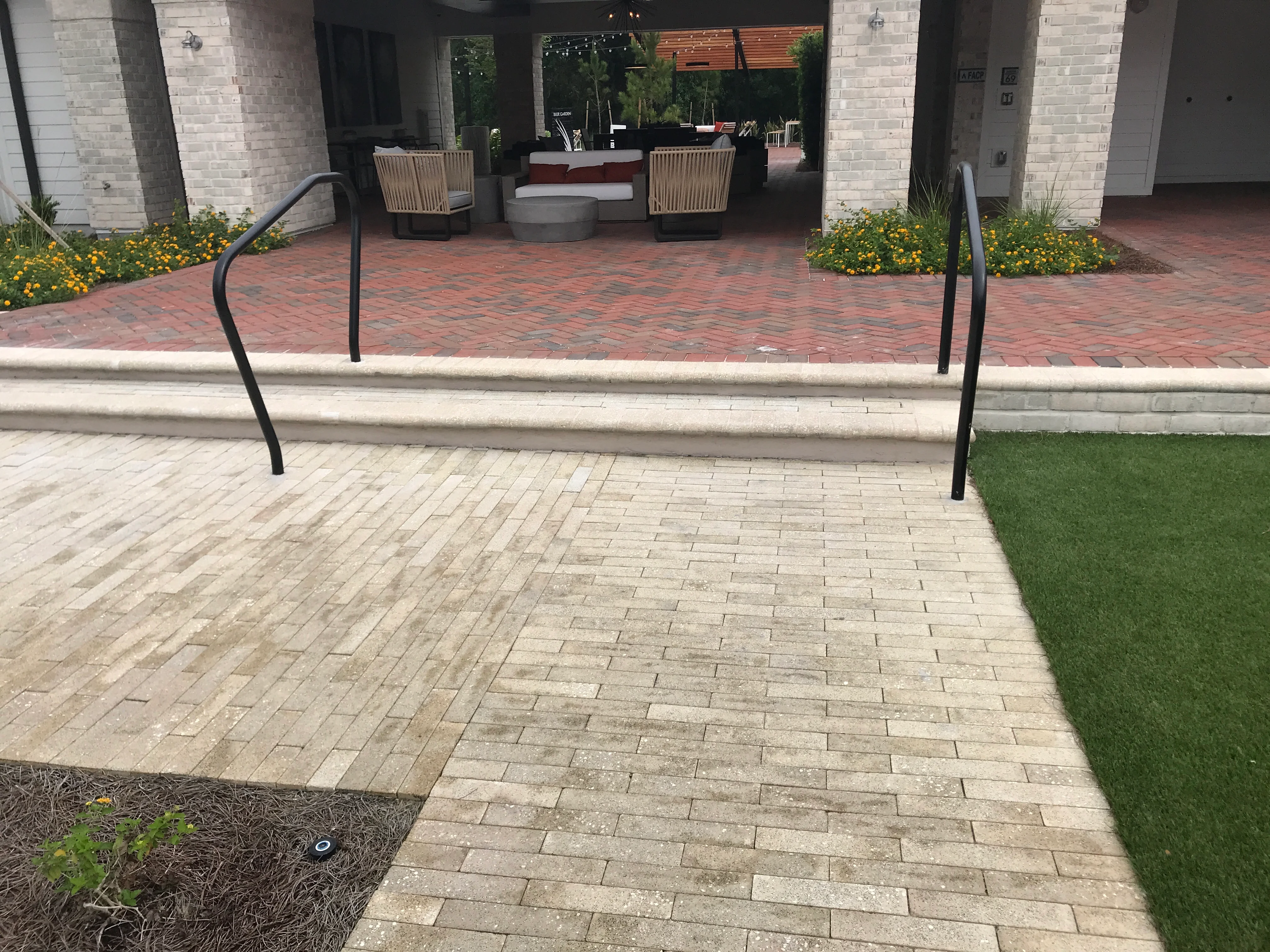 Newly installed paver patio with metal handrails, landscape beds, and sod adjacent to brick building
