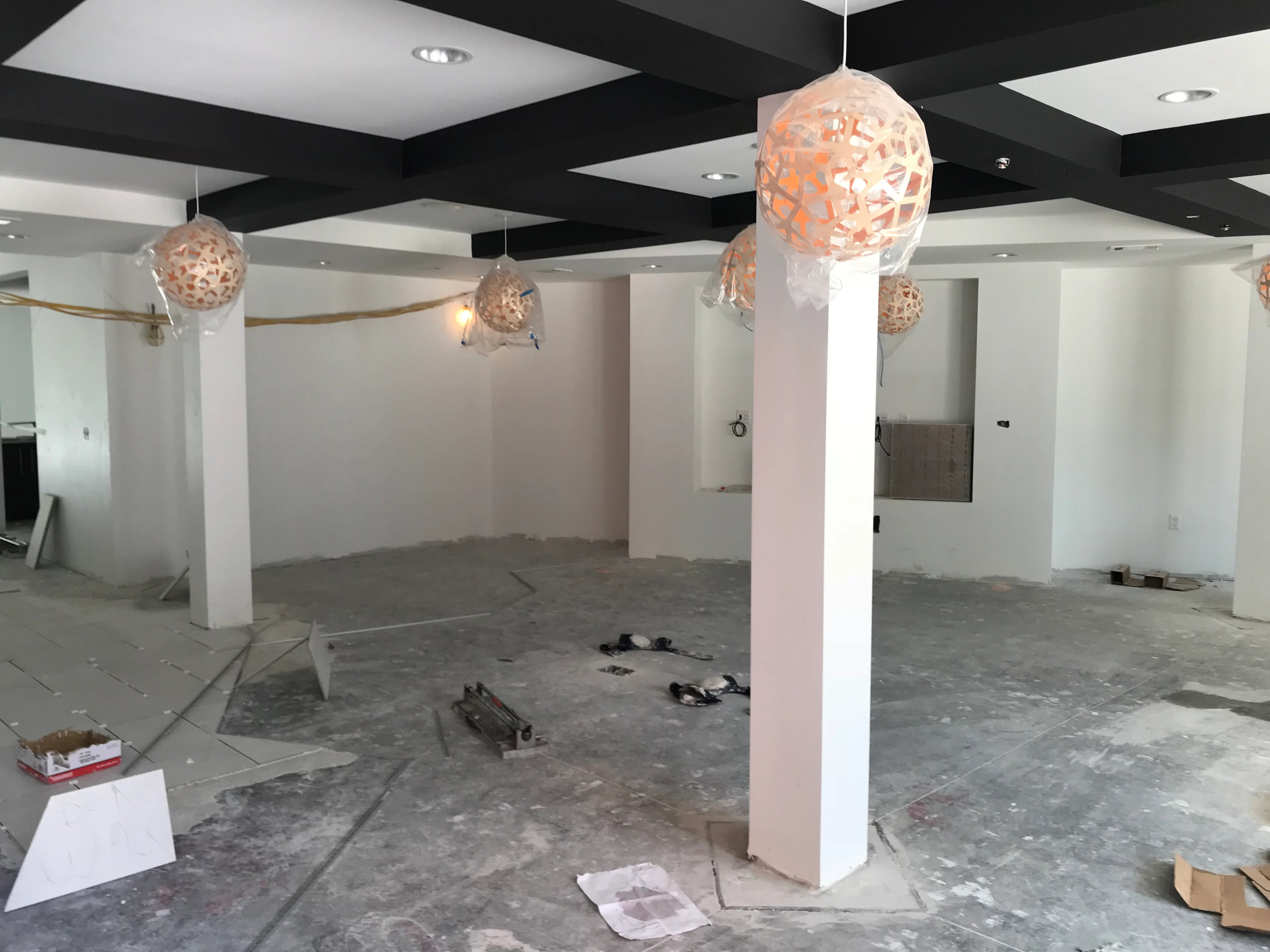 Commercial interior under construction with black coffered ceiling, white columns, and pendant lighting fixtures