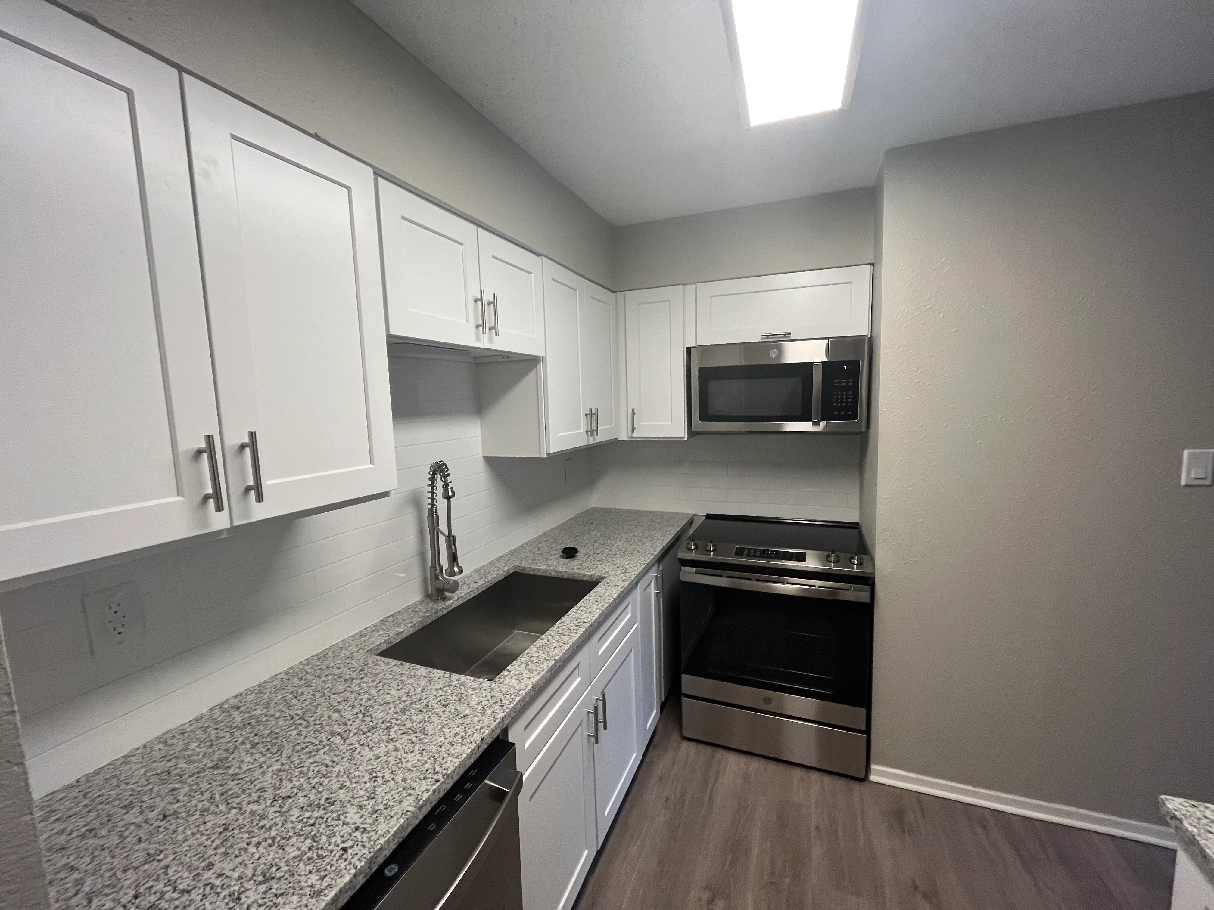 Modern kitchen with white cabinets, gray quartz counters, and stainless steel appliances
