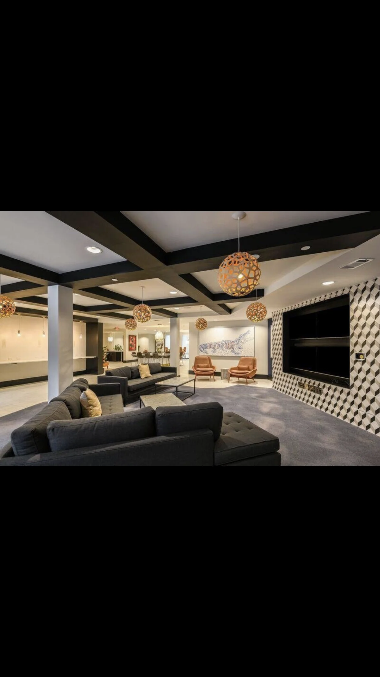 Modern basement with black coffered ceiling, gray seating, and geometric media wall accent