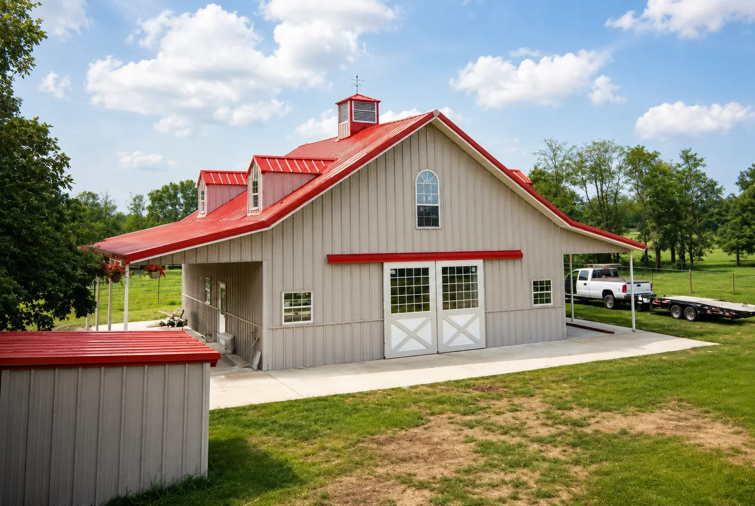 Two-story gray metal barn with red metal roof and white garage doors in rural setting