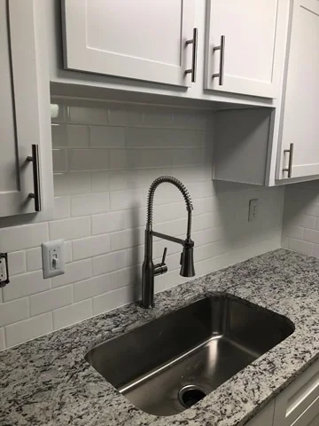 Stainless steel undermount sink with black pull-down faucet, granite countertop, and white subway tile backsplash