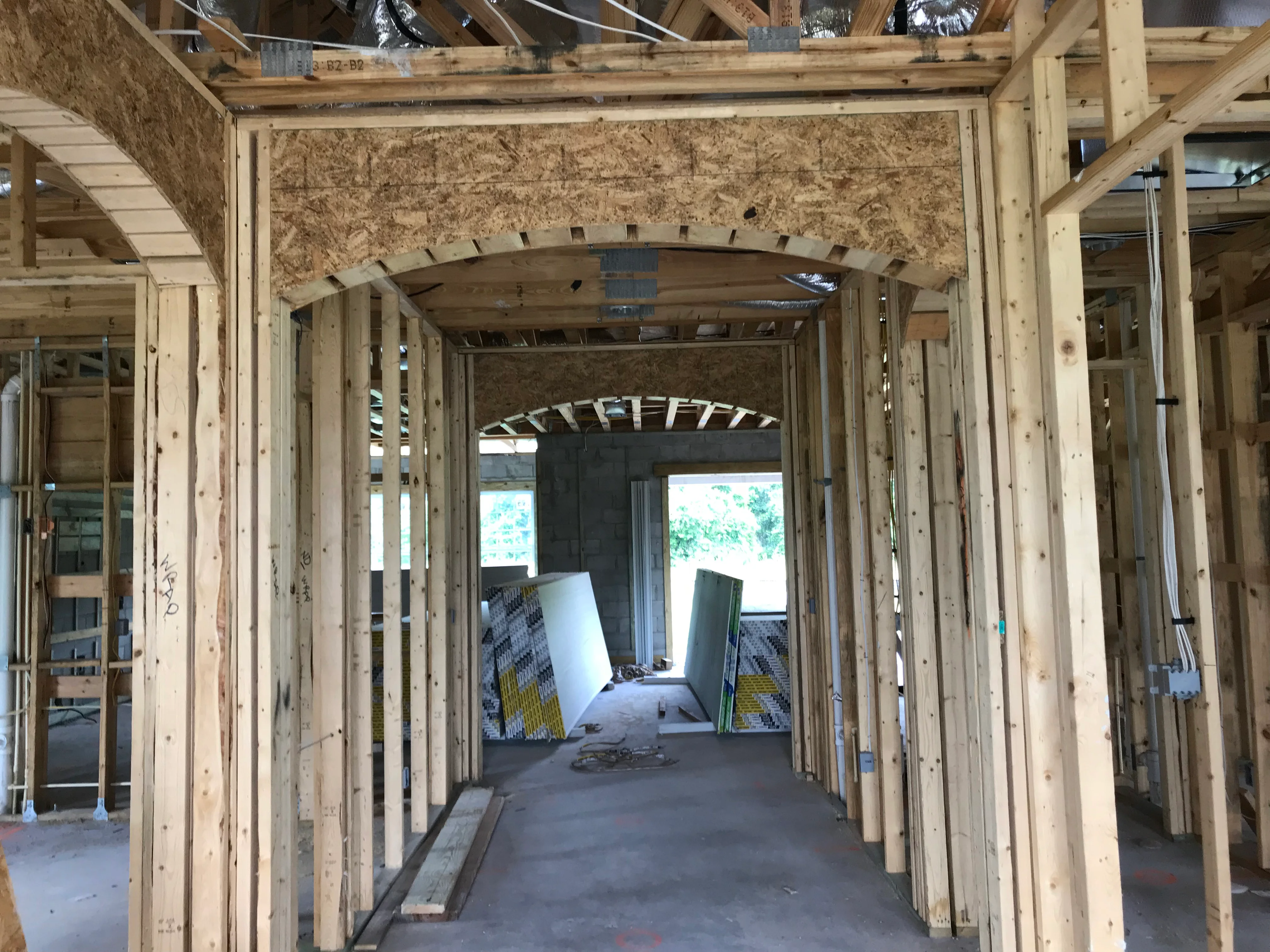 Interior framing with wooden studs, arched doorway openings, and construction materials in progress