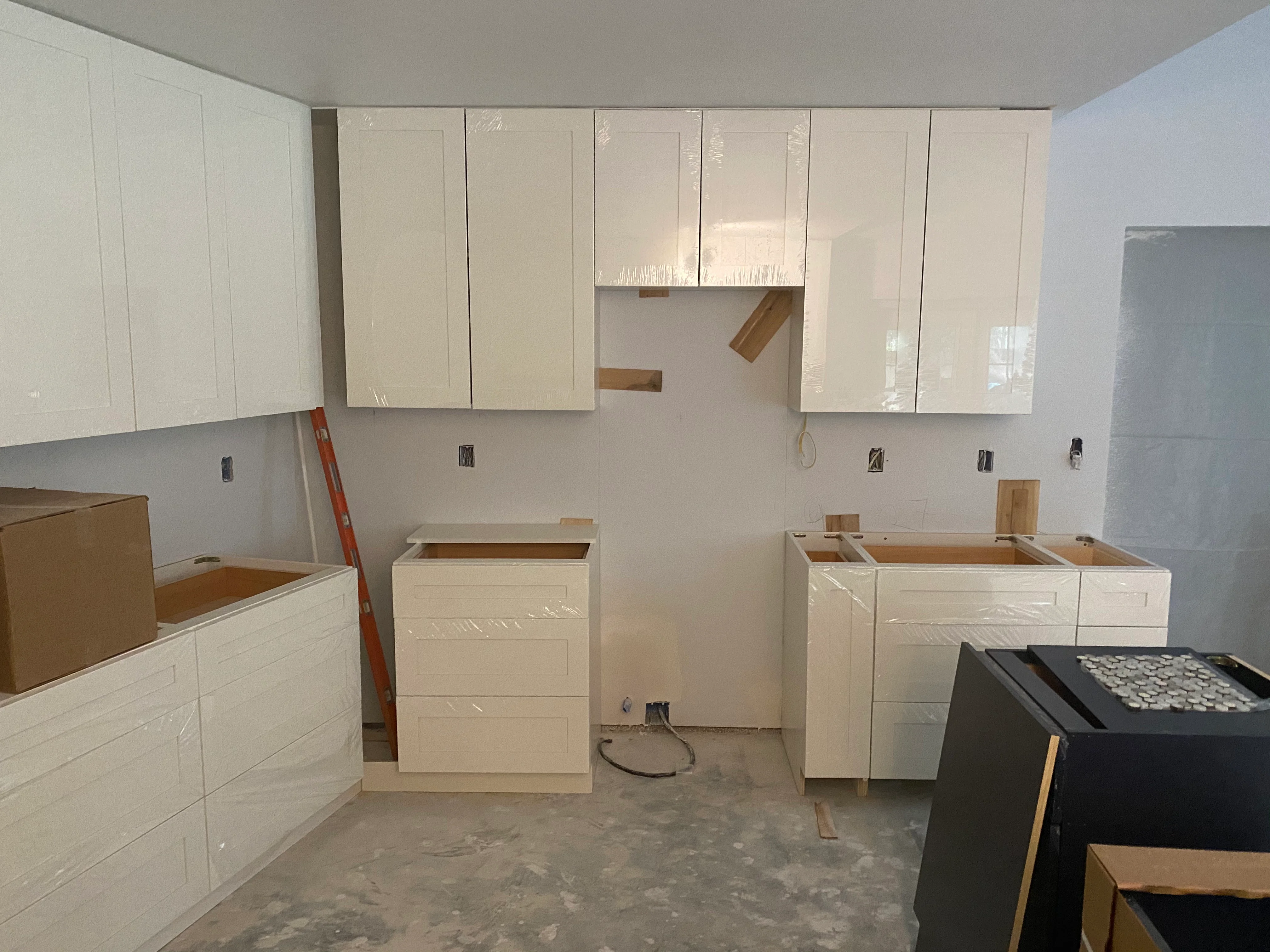 White kitchen cabinets installed in mid-renovation with open boxes and electrical outlets visible