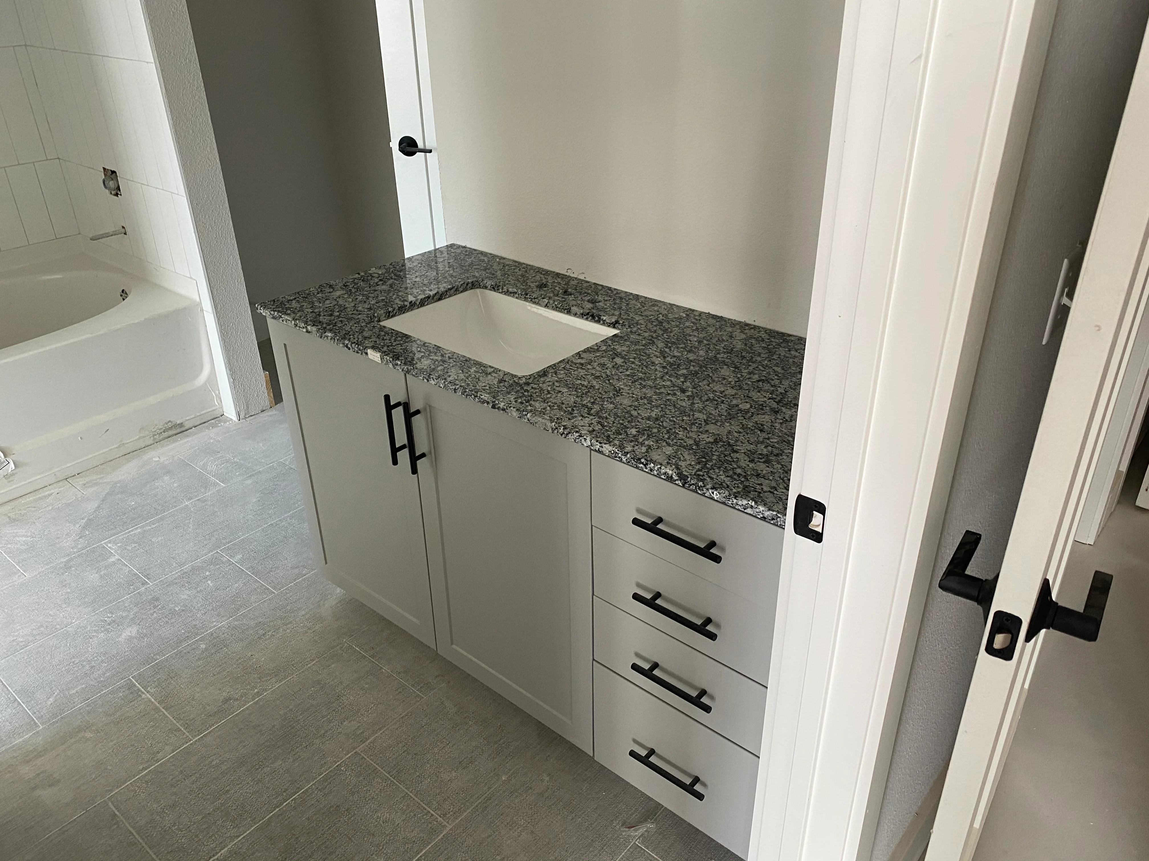 White bathroom vanity with gray granite countertop and black hardware handles