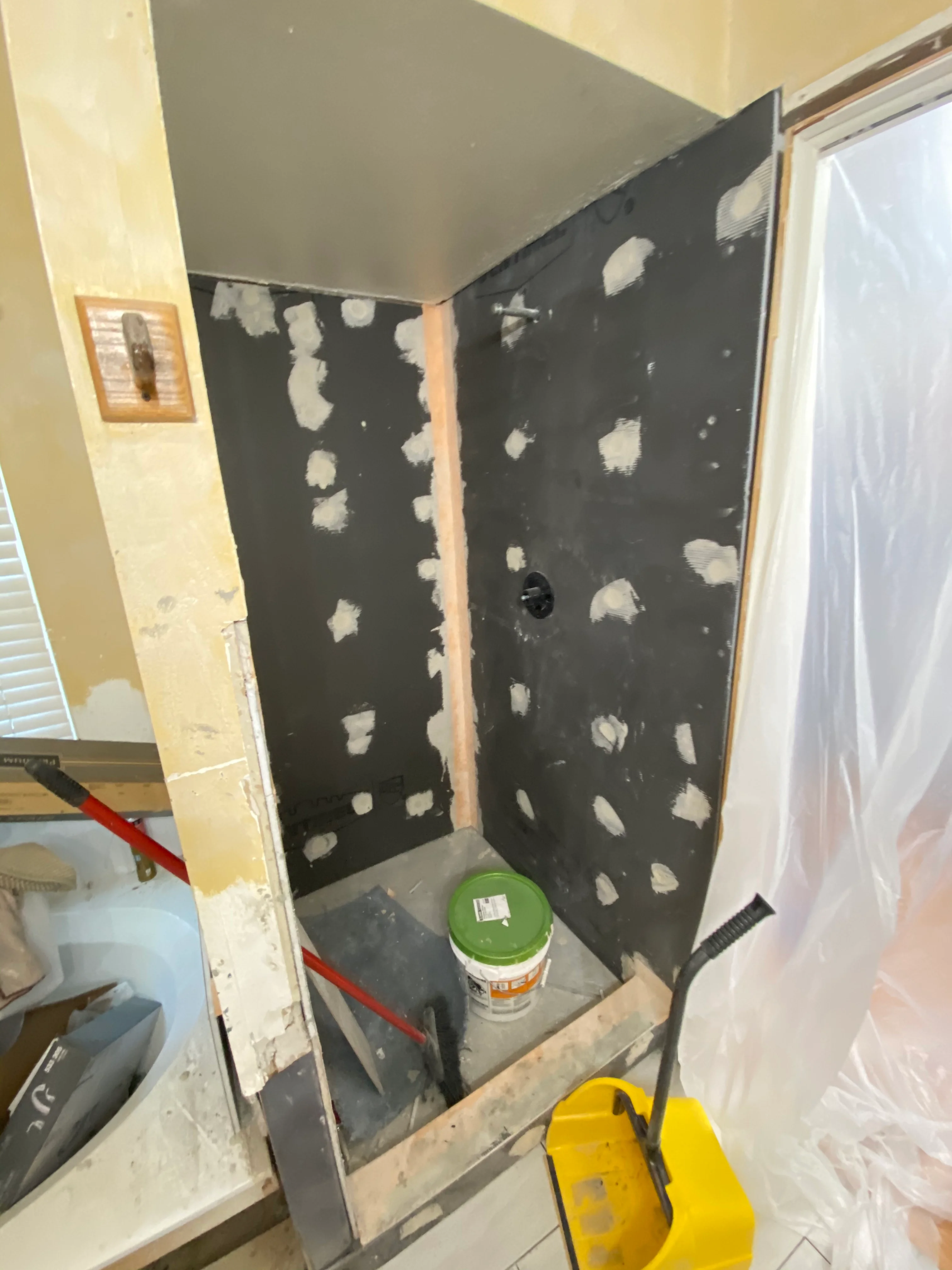 Shower stall under renovation with black waterproof membrane and drywall joint compound