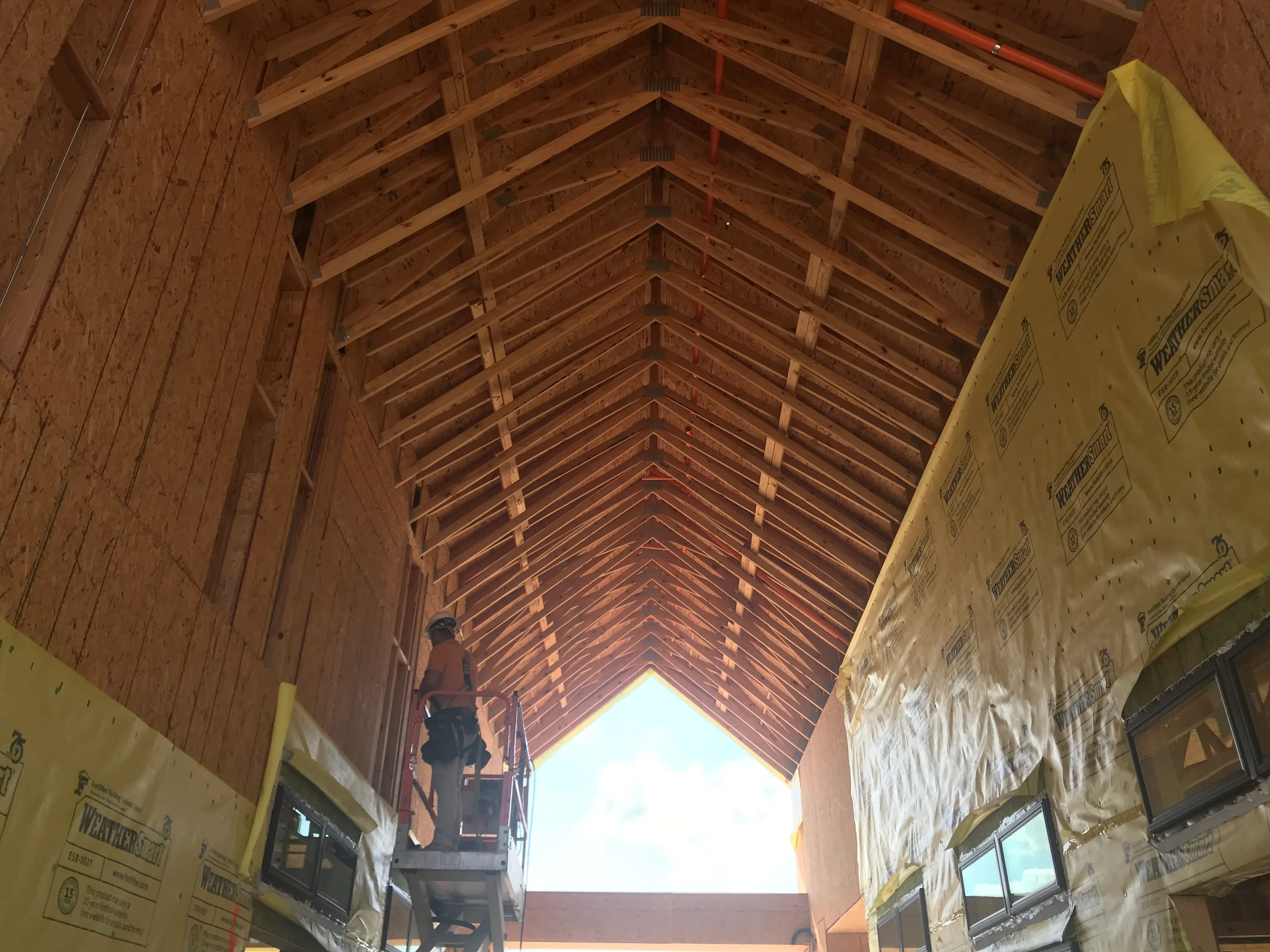 Interior view of wooden roof trusses and framing with yellow house wrap on walls