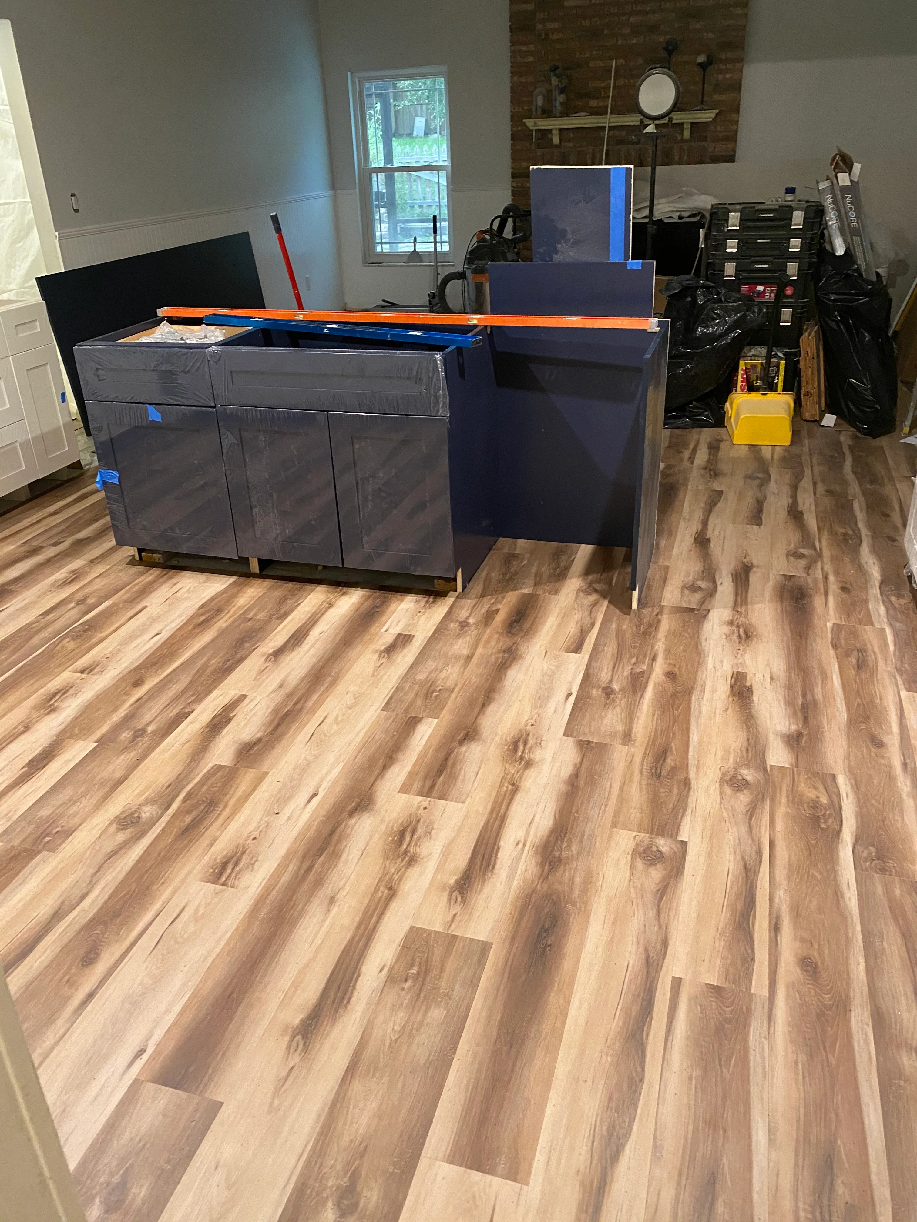 Navy blue kitchen cabinets with orange trim and new wood-tone vinyl plank flooring installation