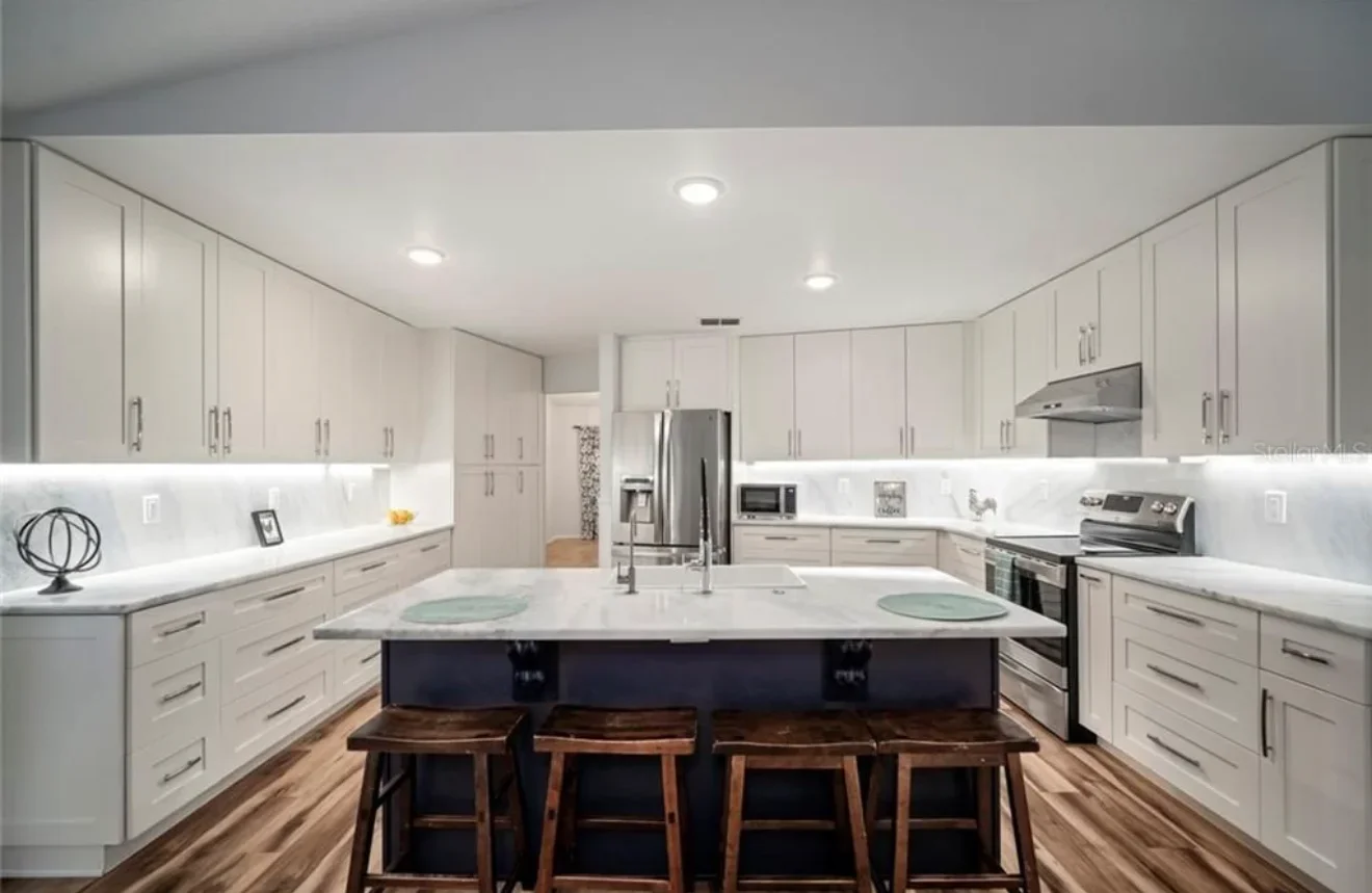 Modern kitchen with white cabinetry, white quartz counters, and dark two-tone island with seating