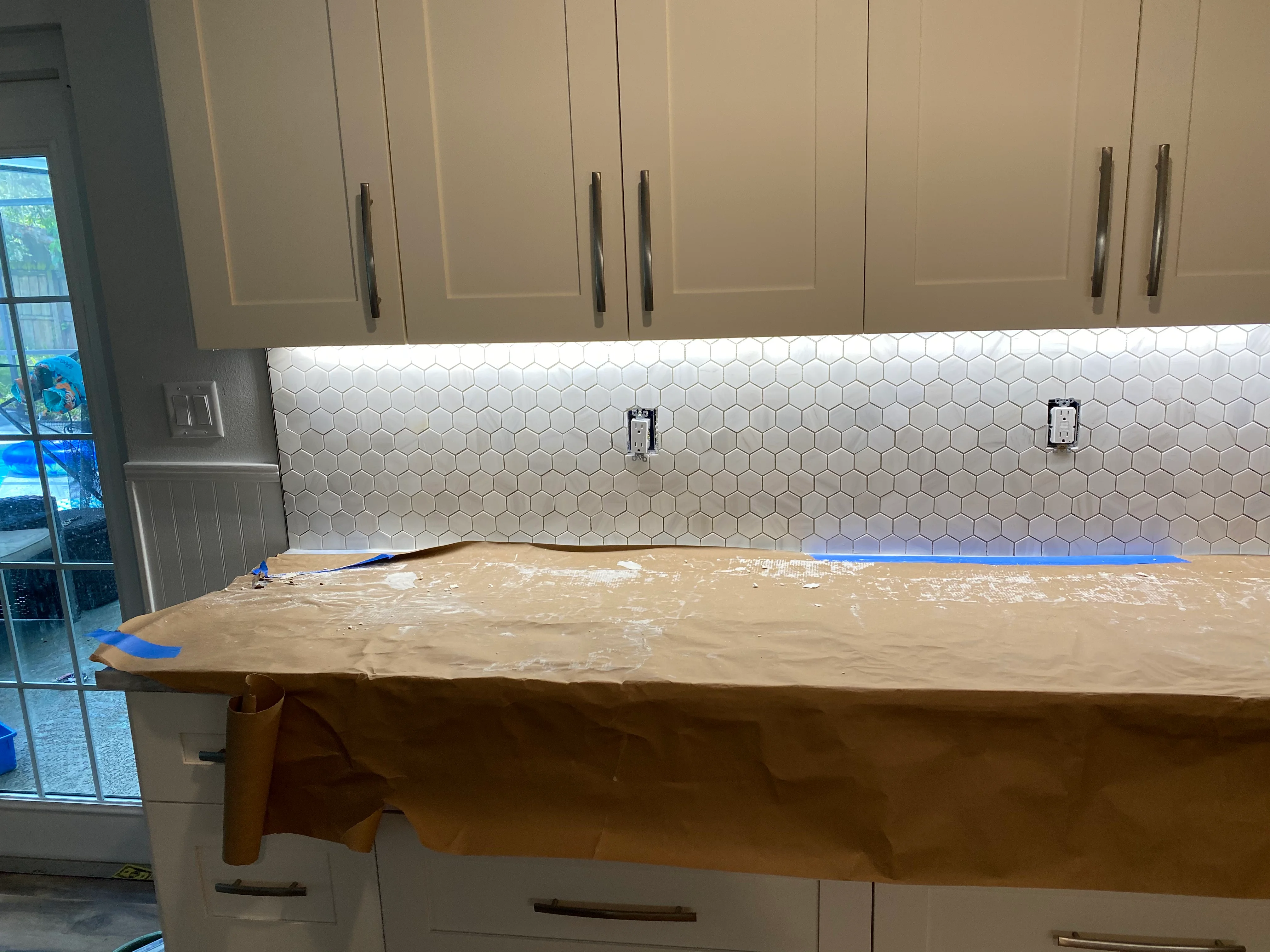 Kitchen remodel in progress with white hexagonal backsplash tile and stone countertop