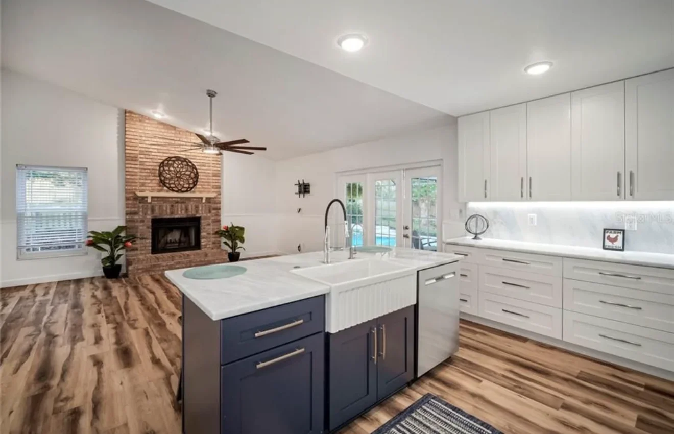Modern kitchen with white cabinets, navy island, and brick fireplace in open-concept home