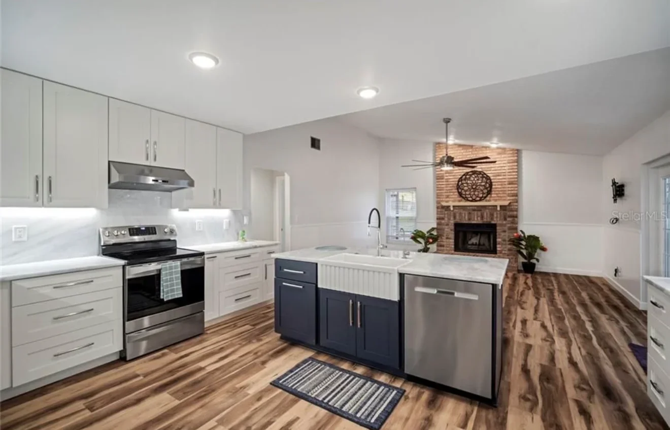 Modern kitchen with white cabinets, navy island, stainless steel appliances, and brick fireplace