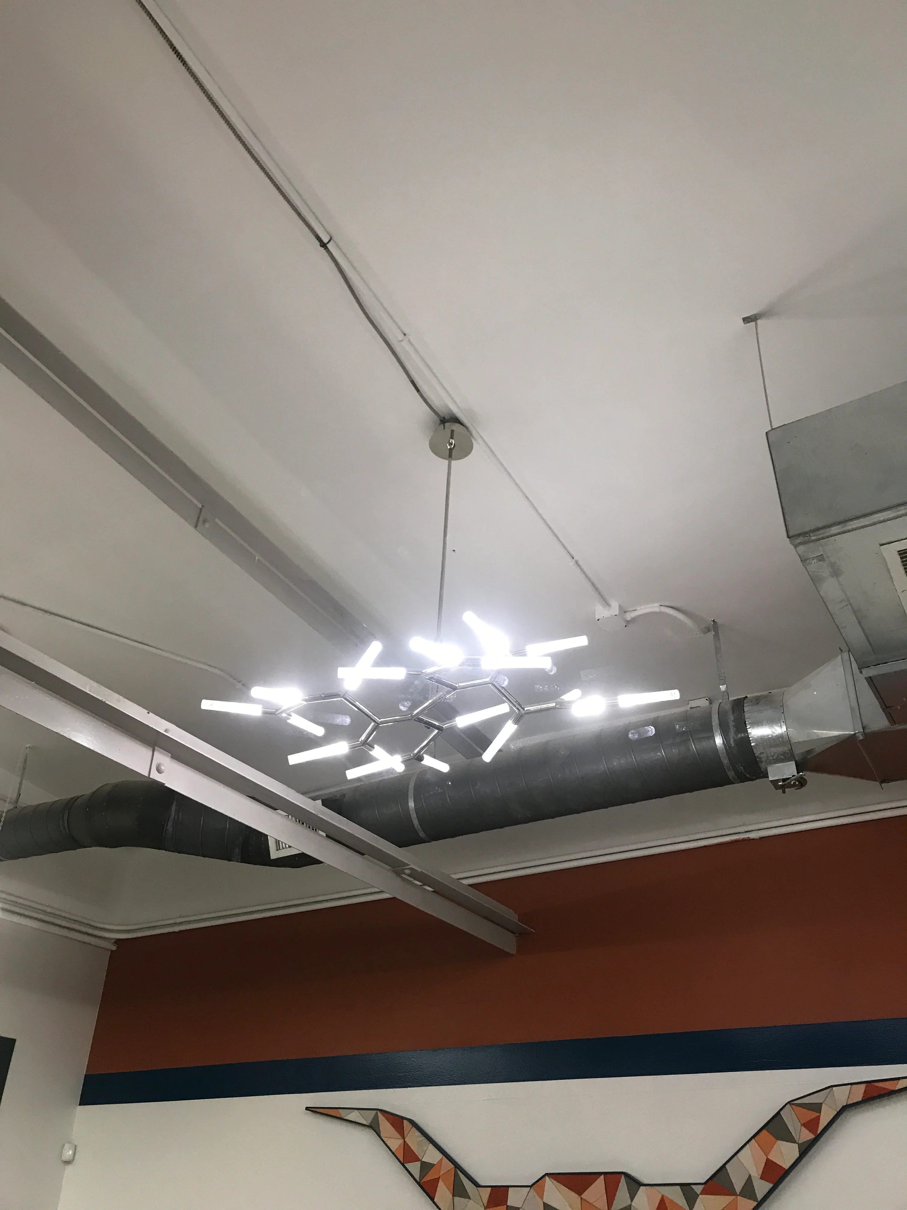 Modern LED pendant lights suspended from HVAC ductwork in finished commercial ceiling