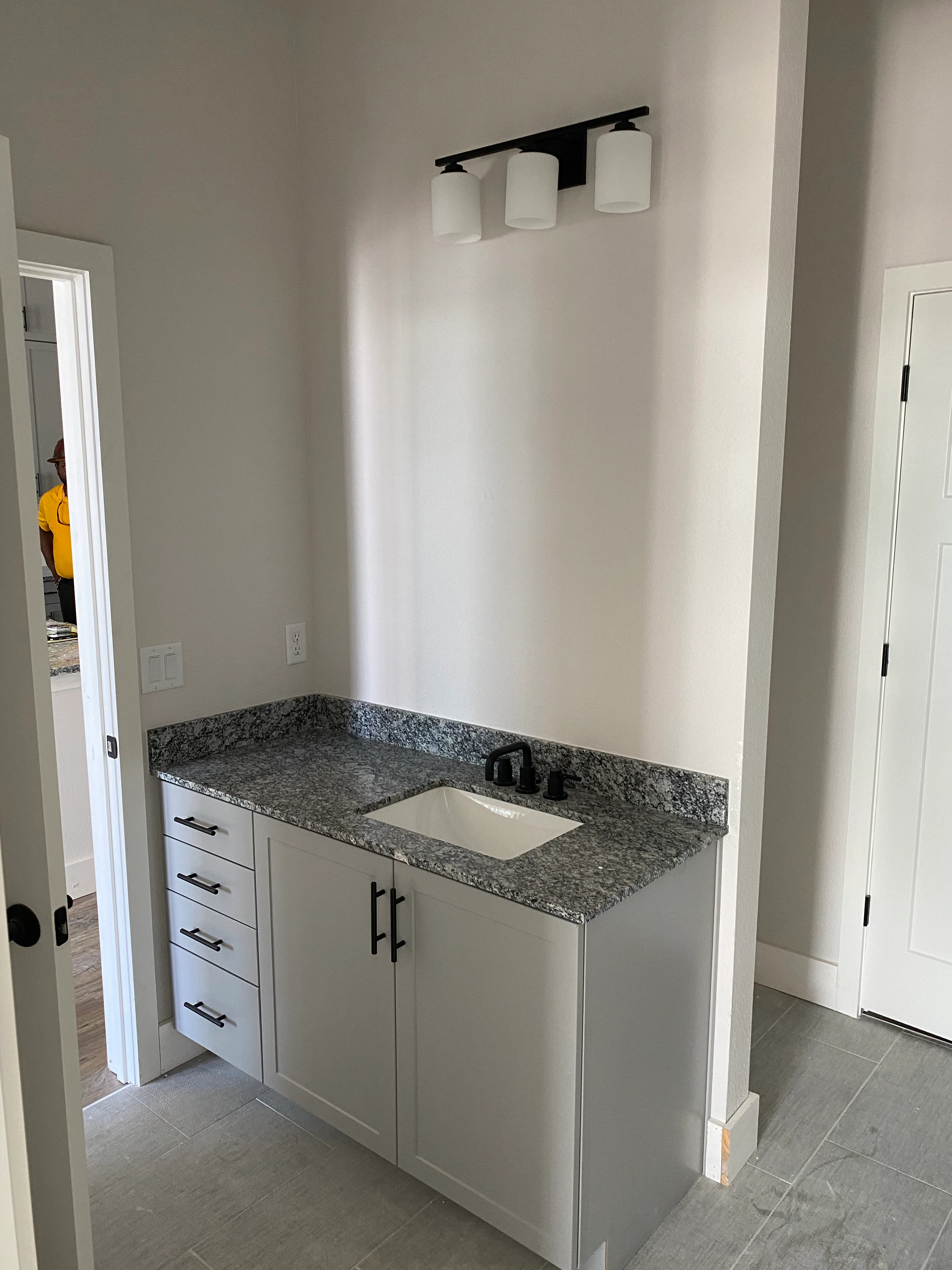 White bathroom vanity with granite countertop, undermount sink, and black metal lighting fixture