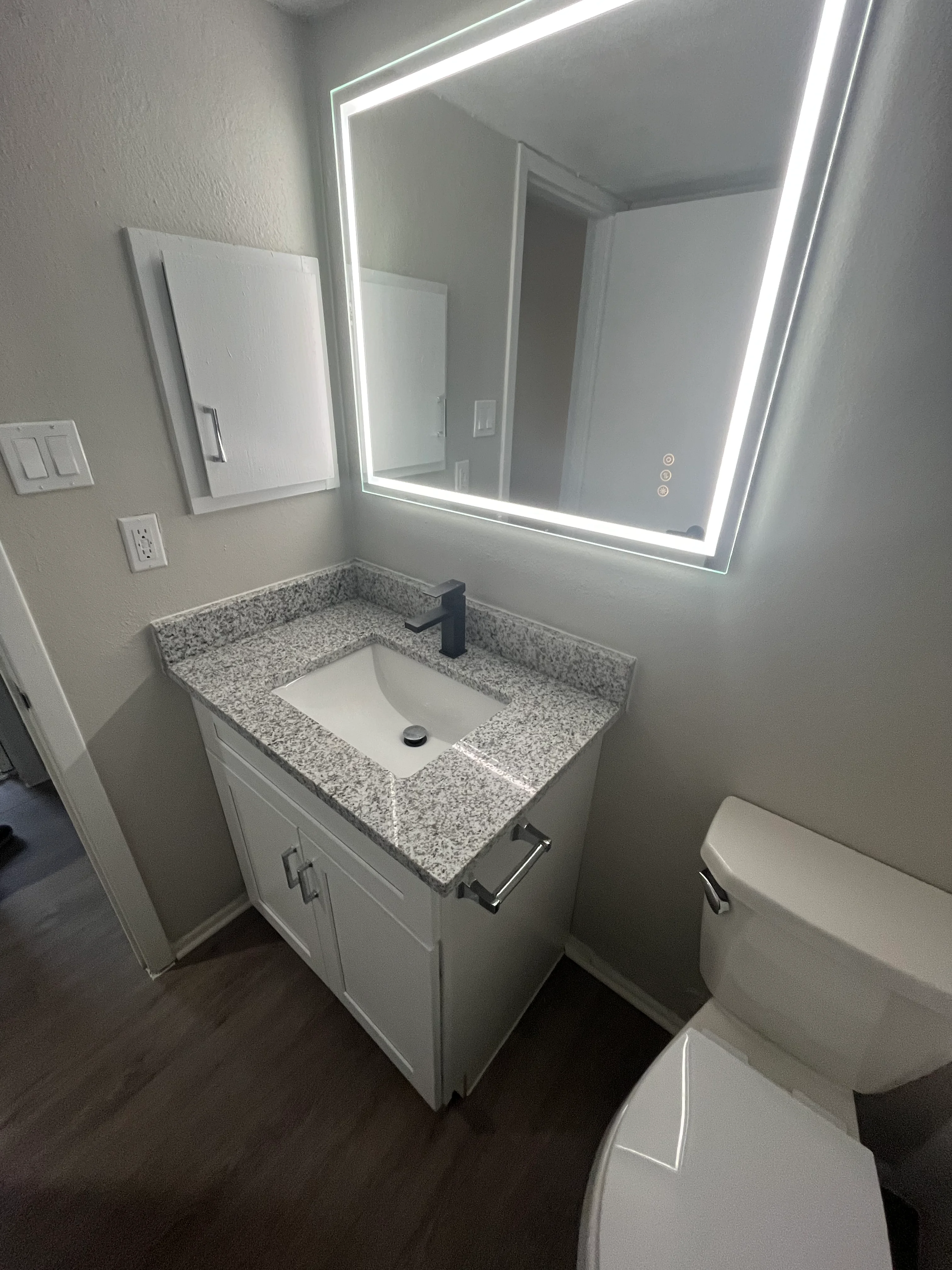 Modern bathroom vanity with granite countertop, white cabinets, and LED-lit mirror