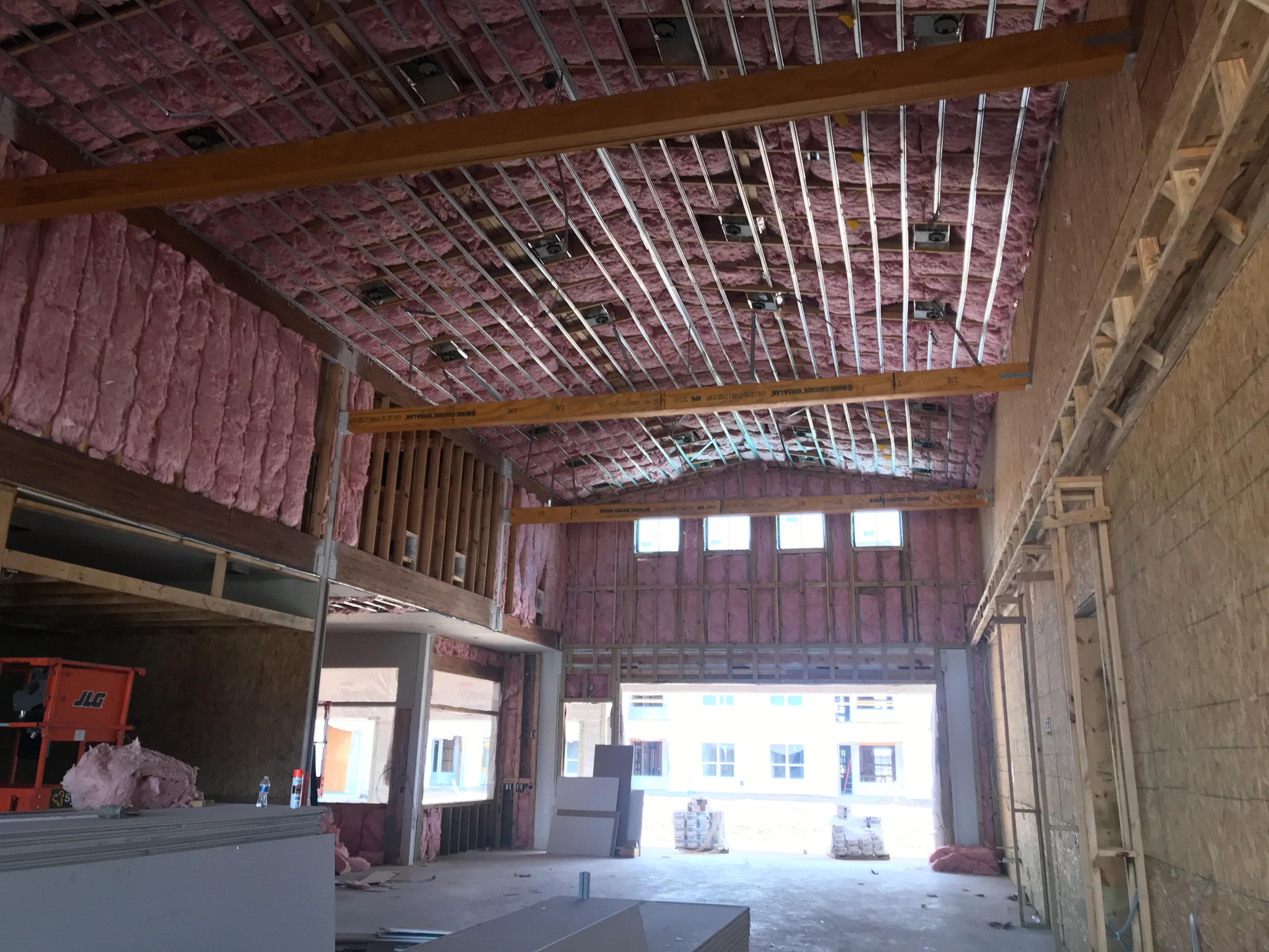 Commercial interior under renovation with exposed framing, pink insulation, and wooden support beams