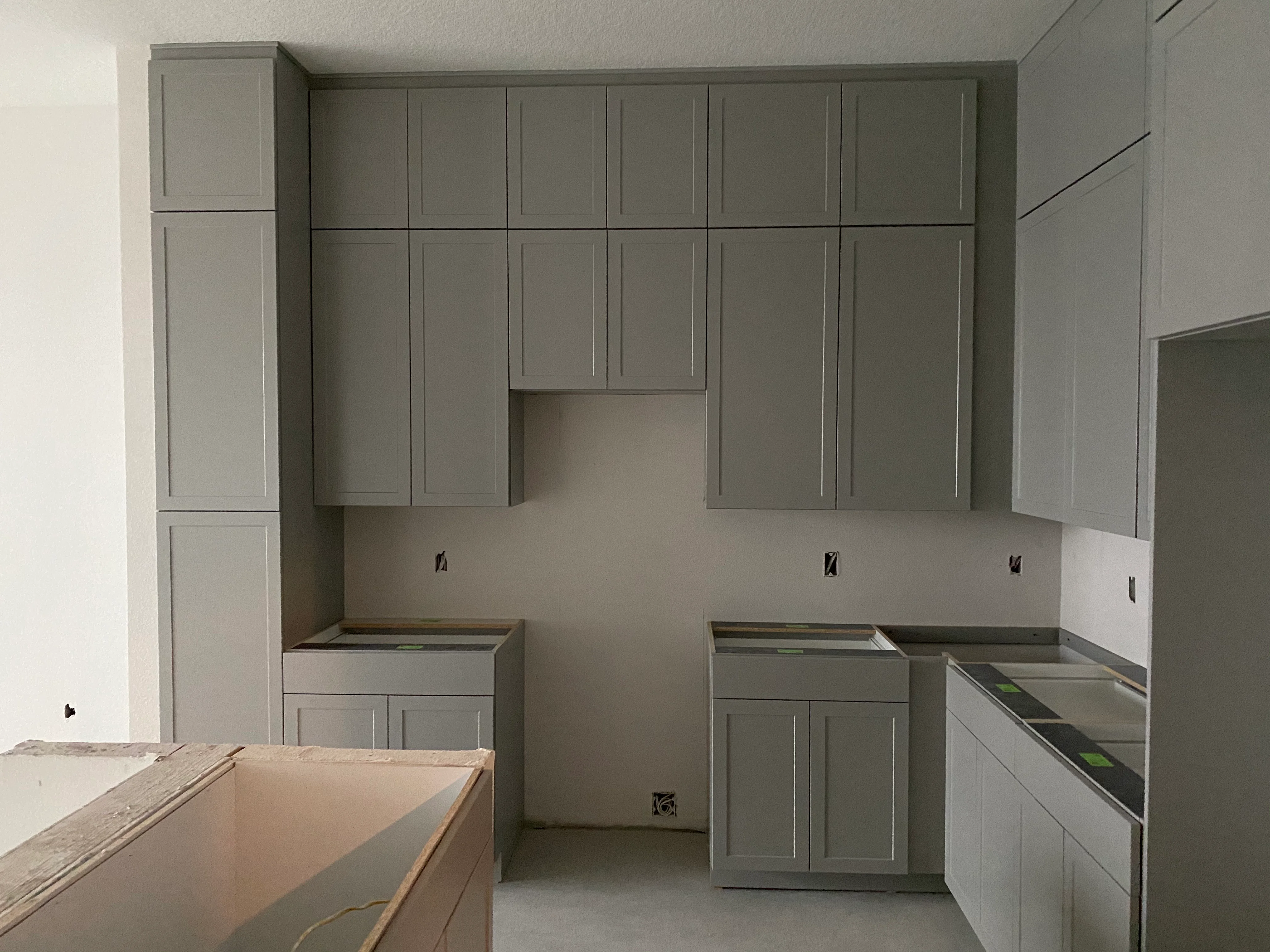 Sage green kitchen cabinets with recessed panels and open shelving during installation