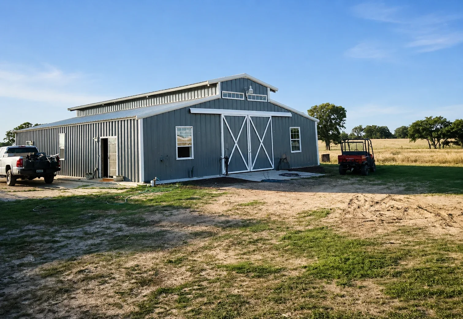 Modern metal barn with blue corrugated siding, white X-pattern doors, and workshop addition on rural property