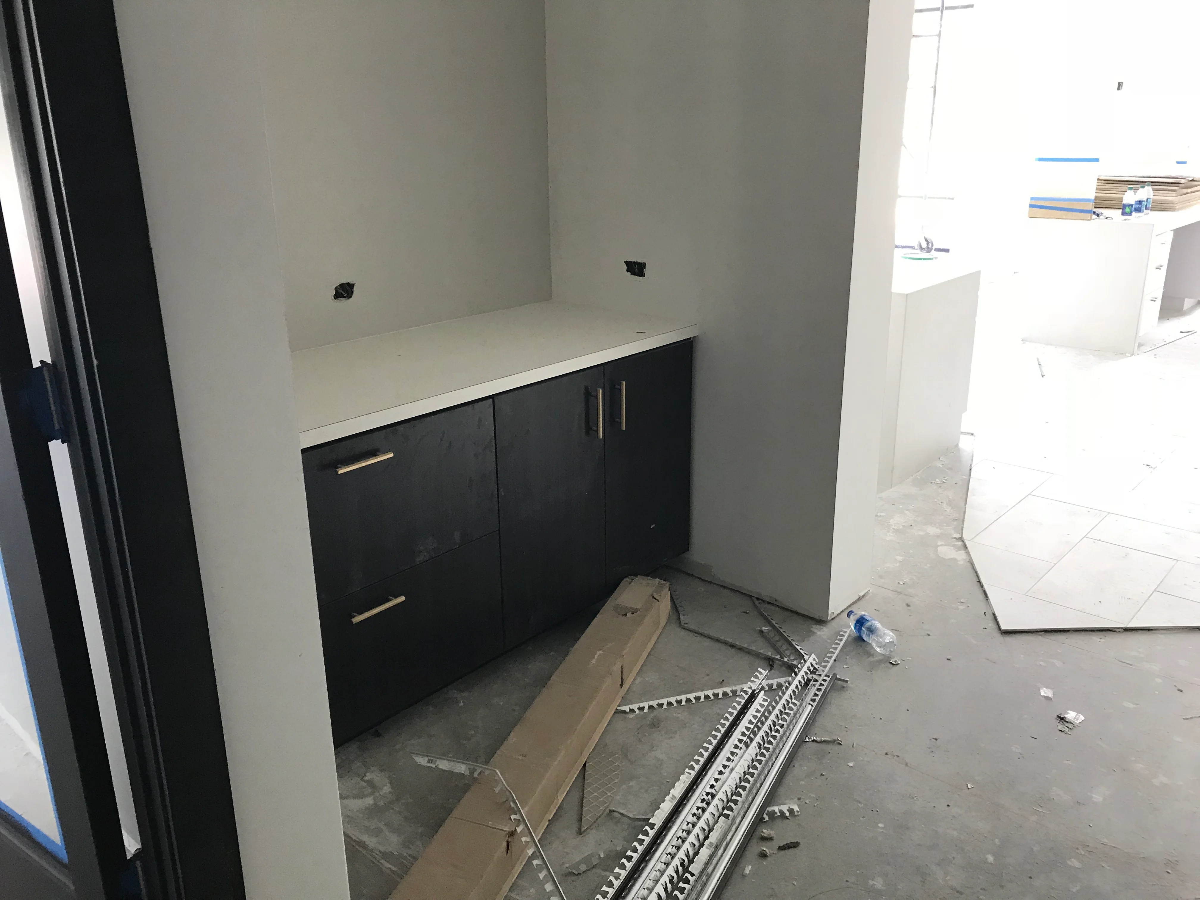 Black kitchen vanity with white countertop installed in drywall alcove during construction