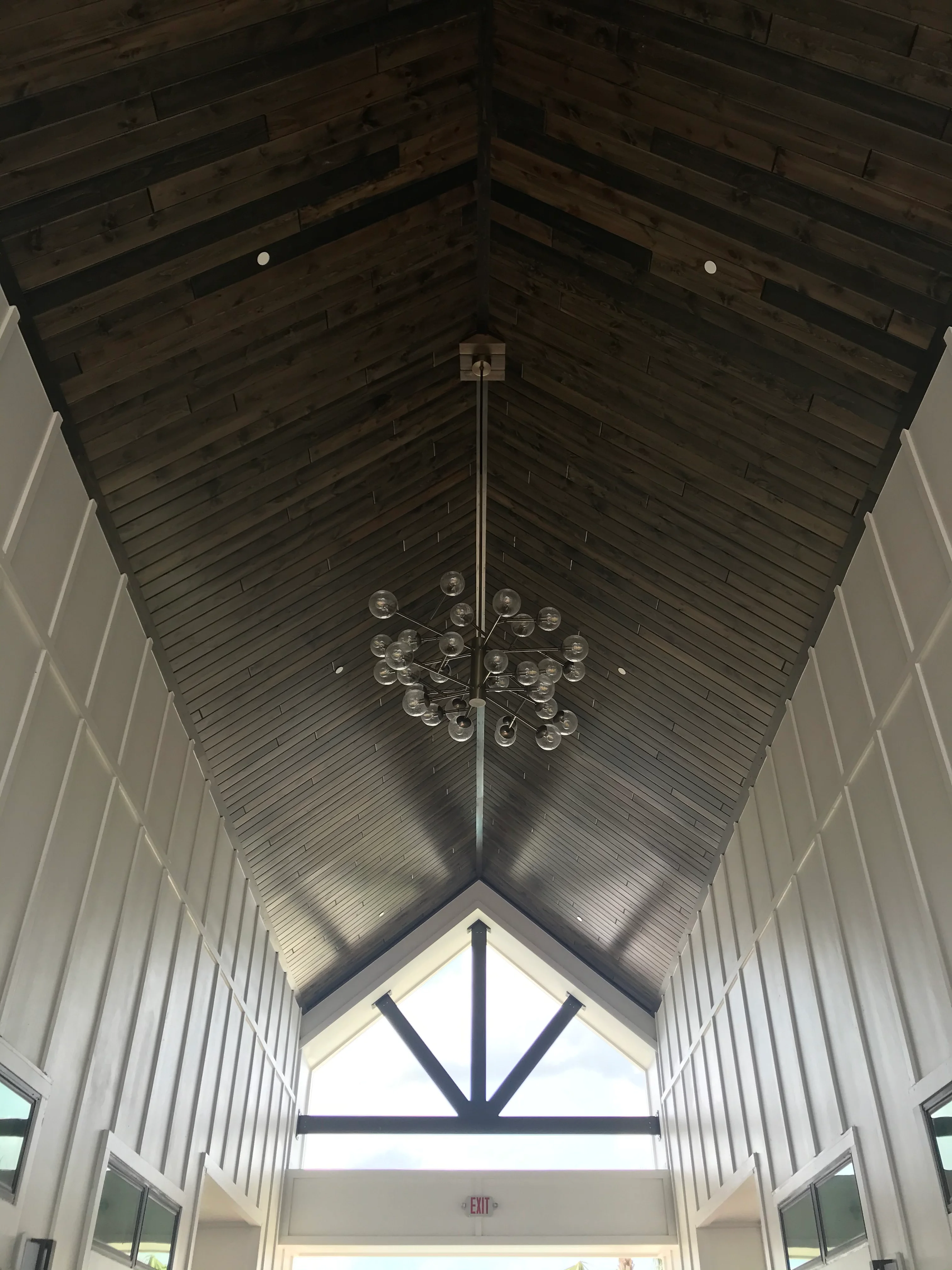 Vaulted ceiling with dark wood beams, shiplap interior, and geometric transom window