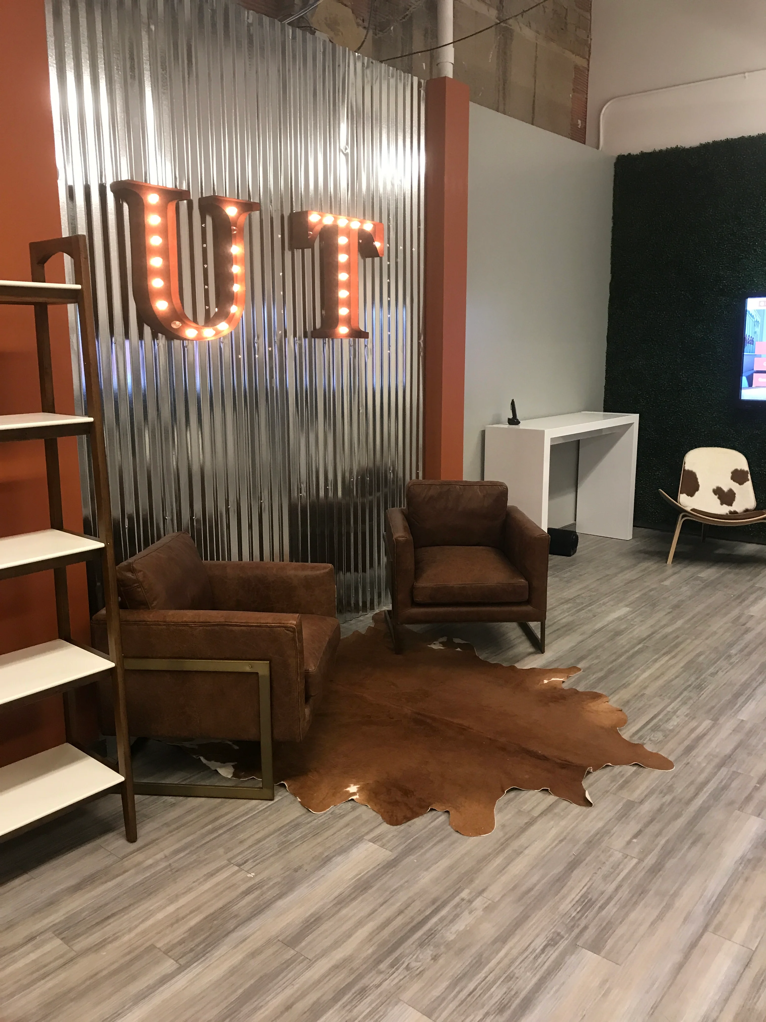 Commercial interior with illuminated signage, brown leather chairs, and corrugated metal wall