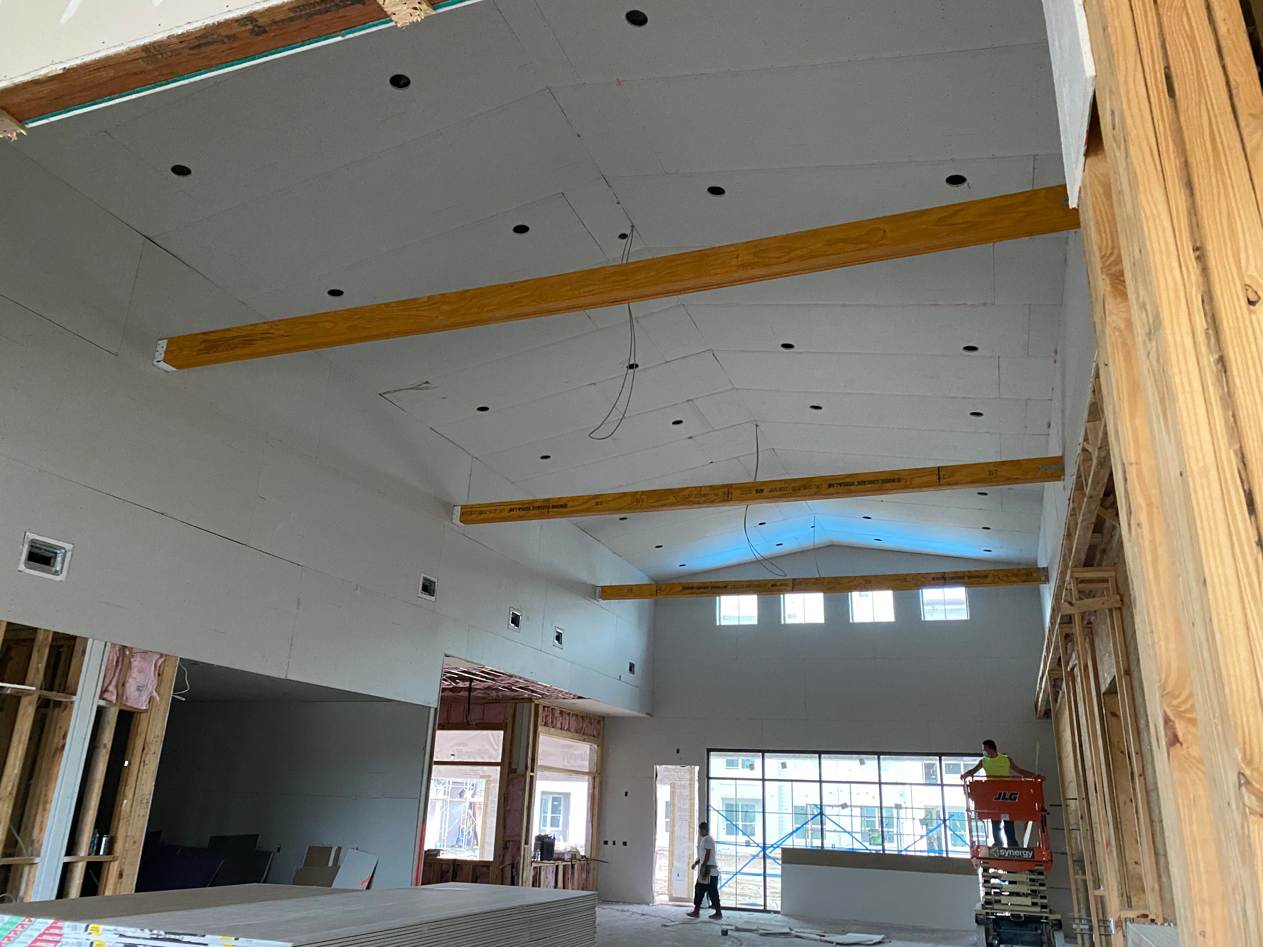 Commercial interior with exposed wood beams, drywall ceiling, recessed lights, and storefront windows under construction