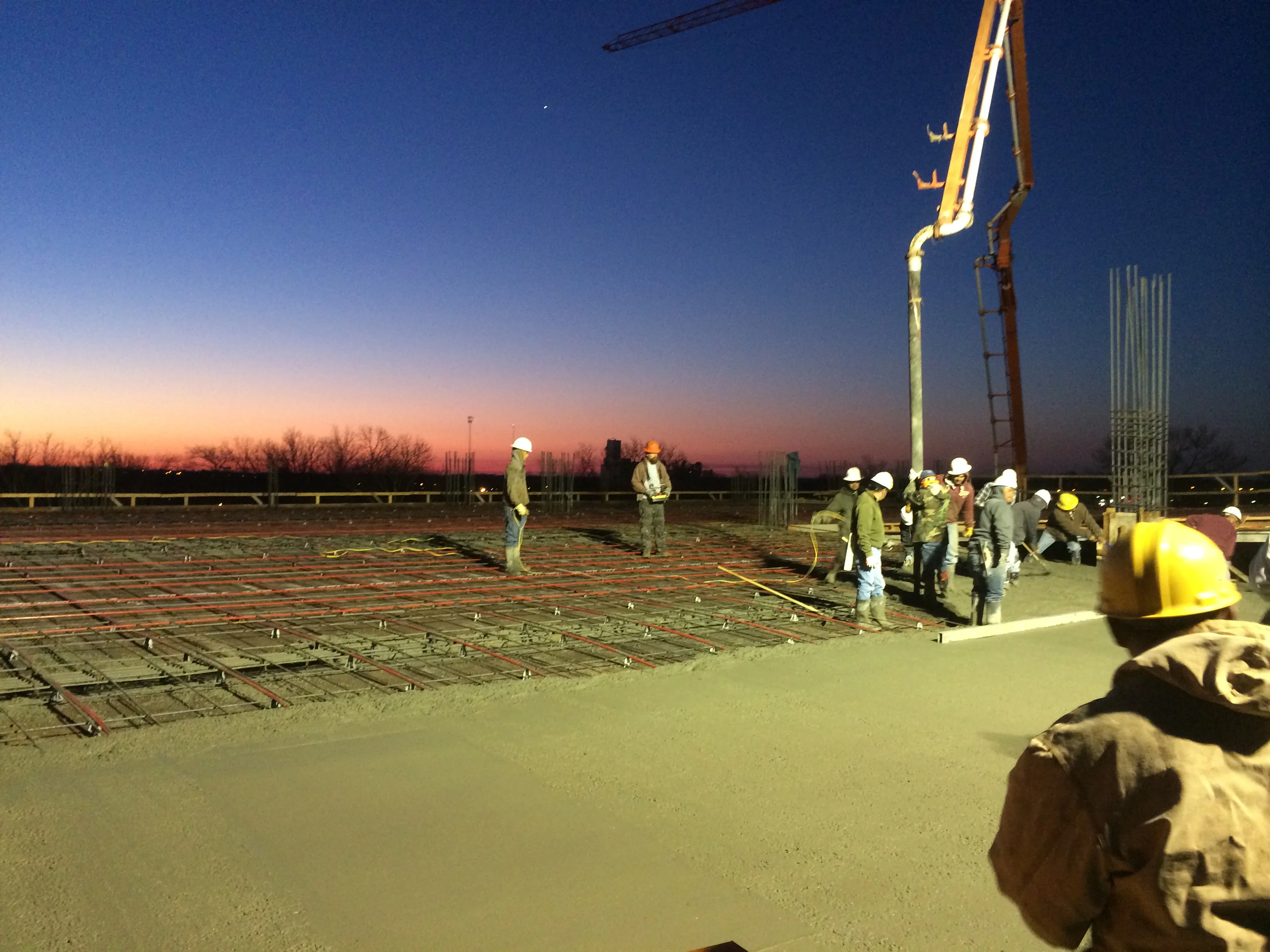 Construction crew pouring concrete foundation with pump truck at sunrise