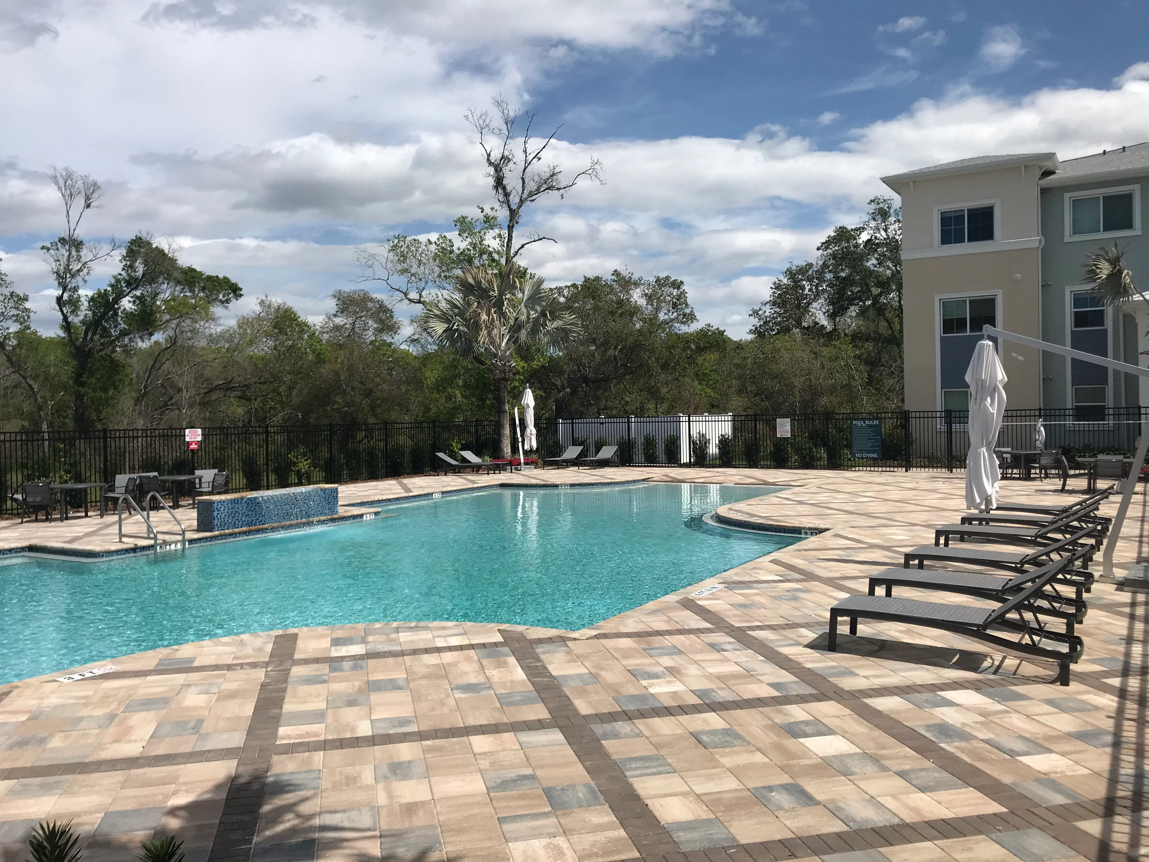 Resort-style community pool with geometric paver deck, lounge chairs, and residential building