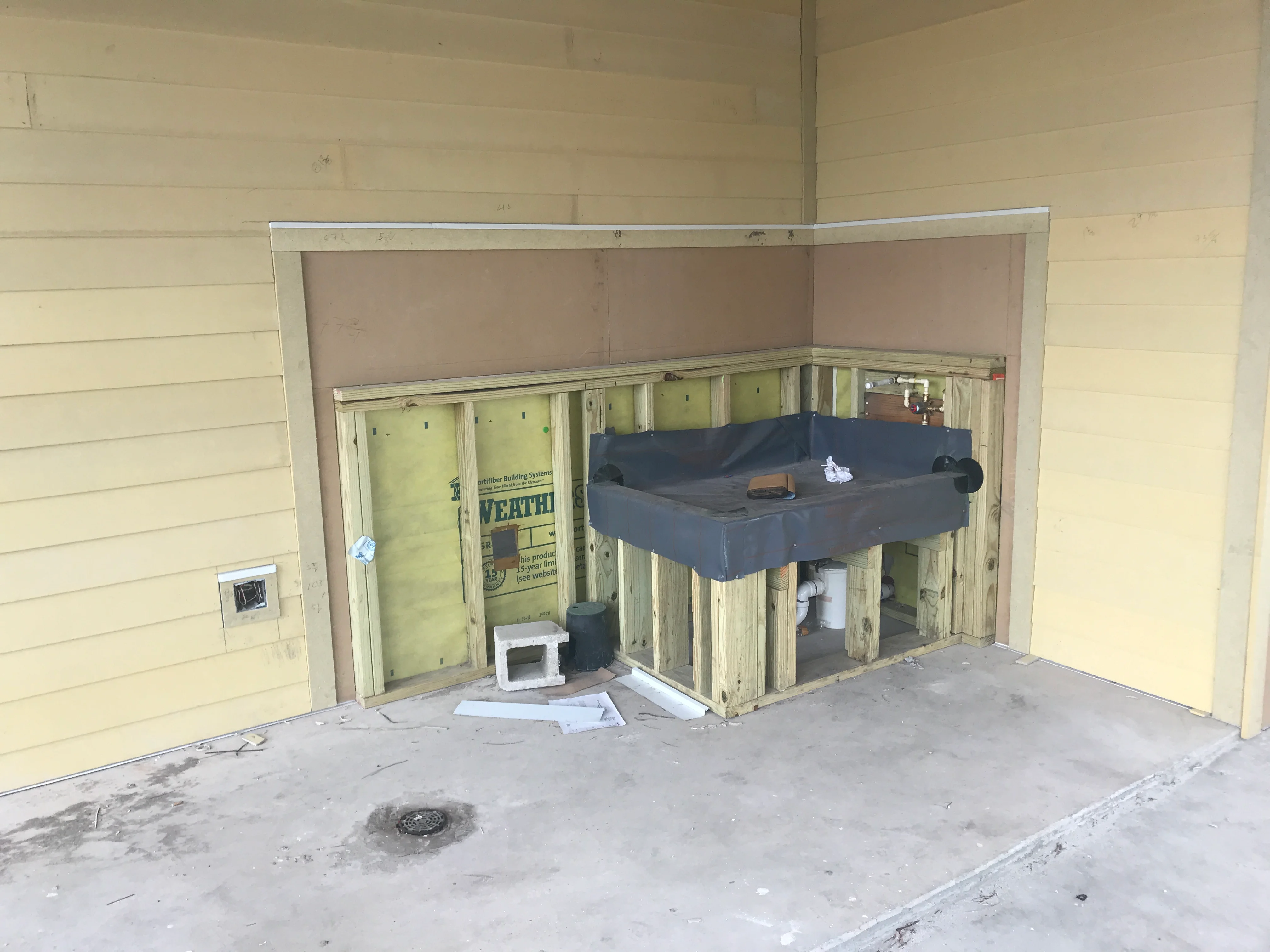 Kitchen framing with yellow insulation, studs, and blue protective covering during construction phase